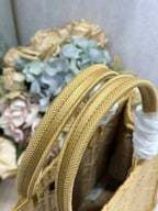 Dior gold handbag close-up of two woven top handles with white tie detail.