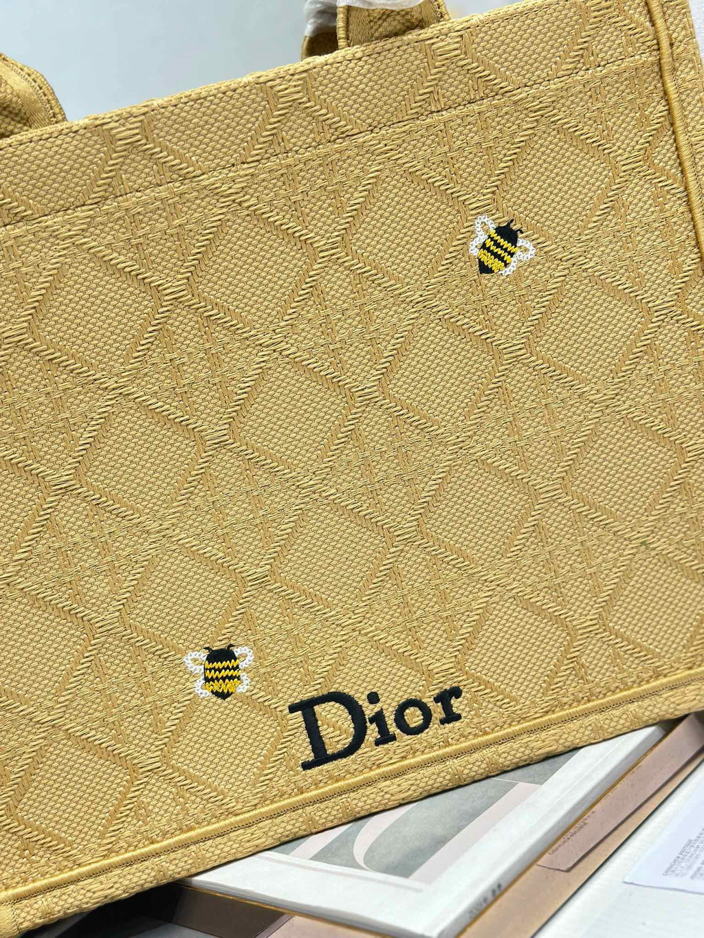 Dior gold handbag close-up of textured fabric, small charm, and Dior logo label.
