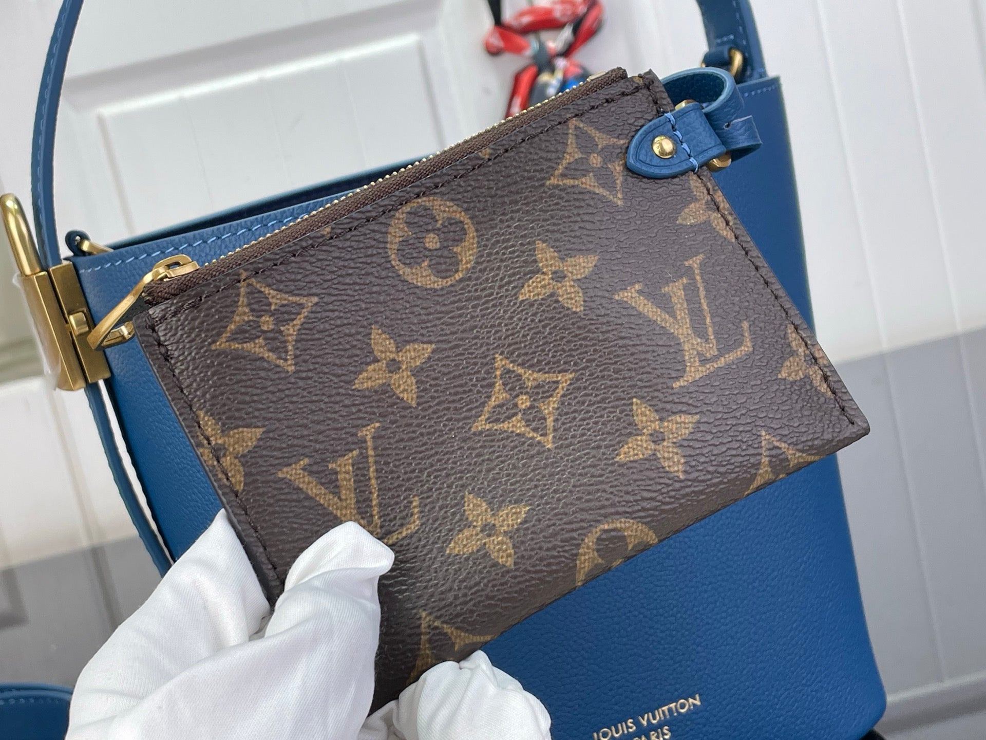Brown monogram pouch with blue strap and gold-tone clasp on blue bag