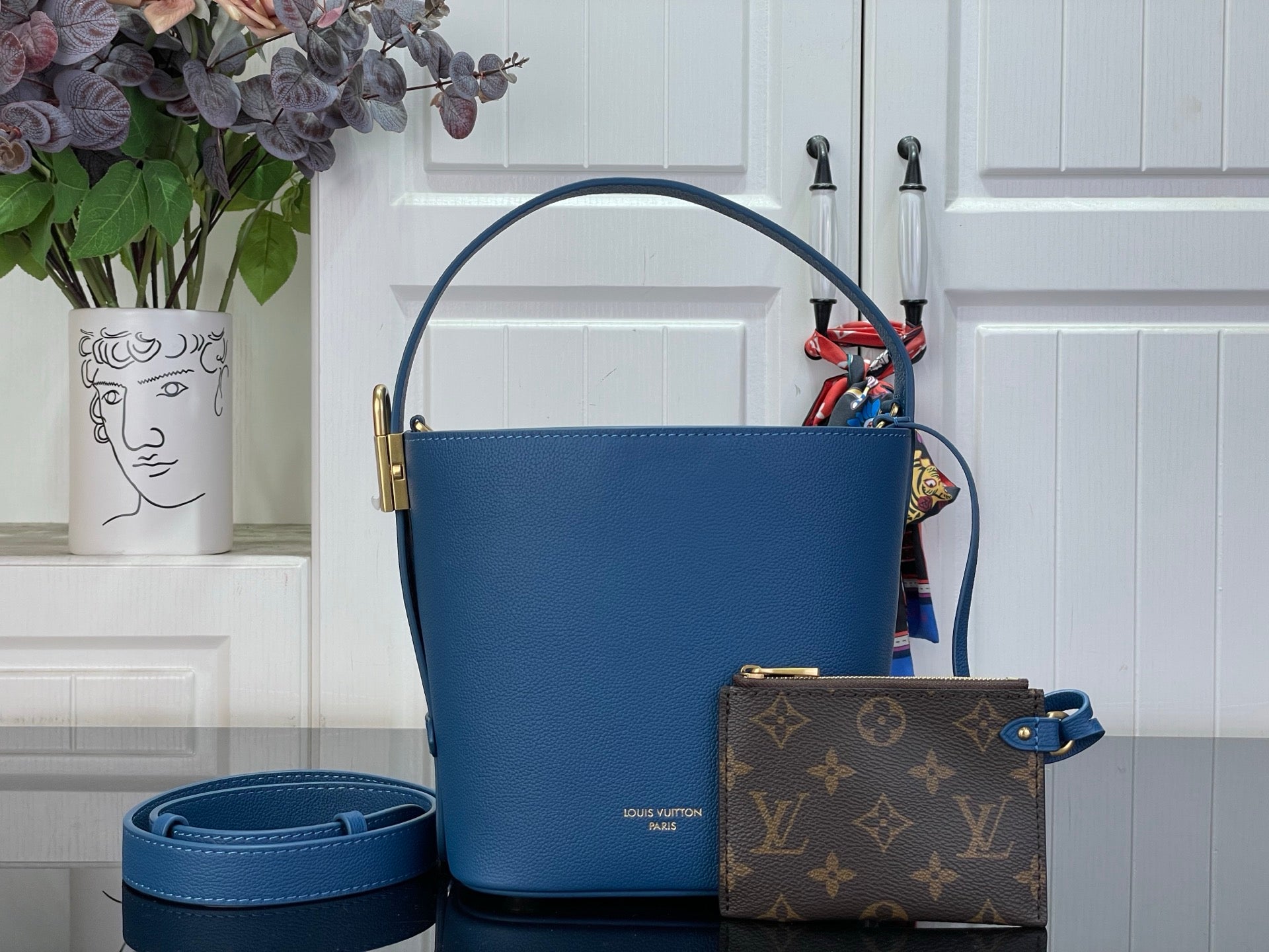 Blue leather bucket bag with gold-tone handles and attached small monogram pouch