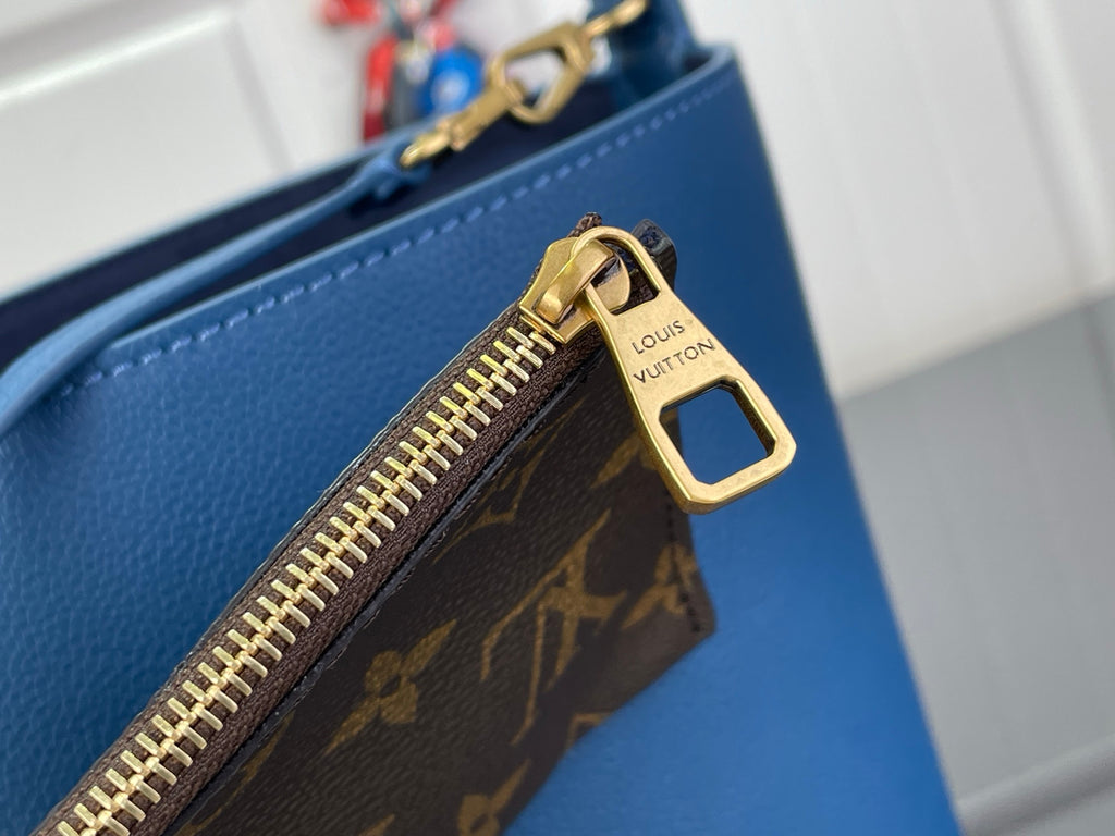 Monogram zipper pocket on blue bag with gold-tone zipper pull