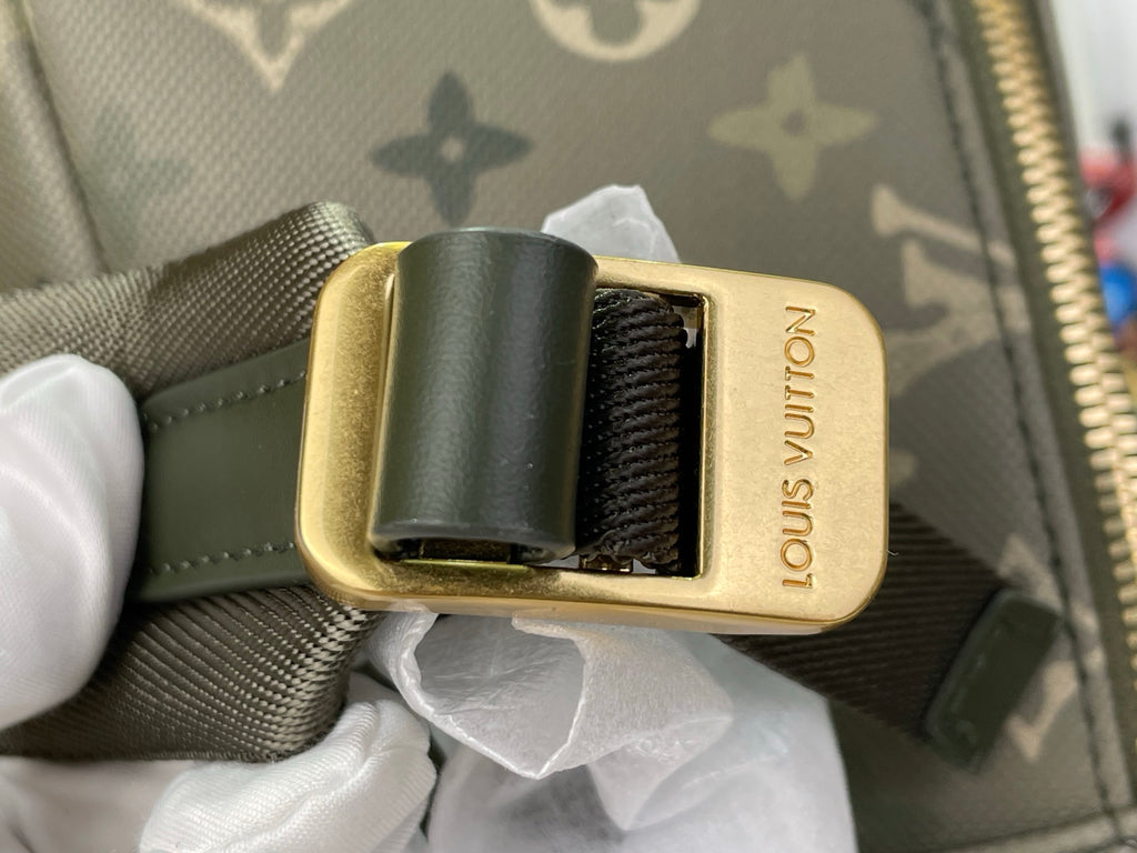 Gold buckle with black strap lining on gray-green monogram backpack
