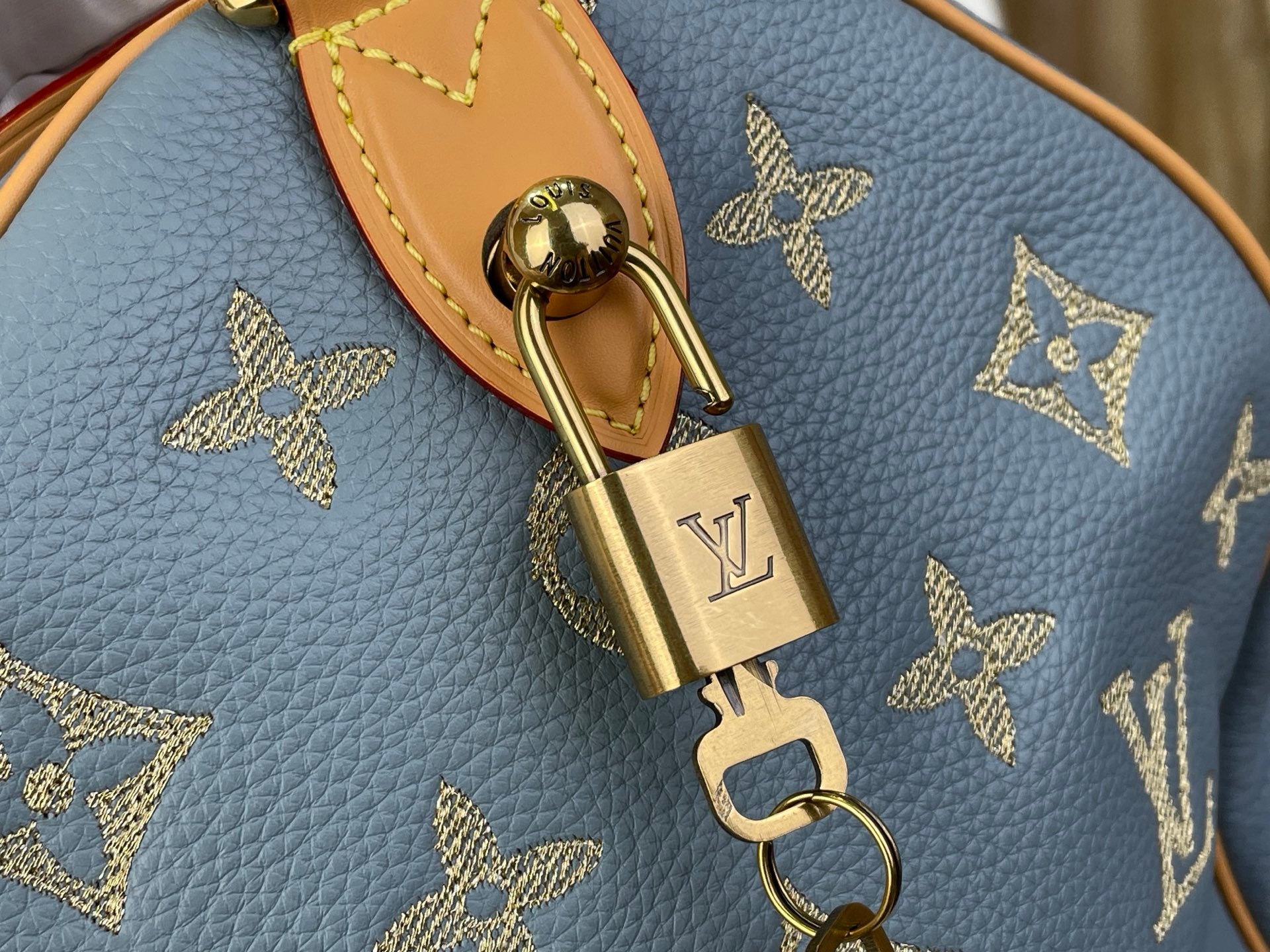 Louis Vuitton gold padlock charm on light blue monogram tote with tan leather strap