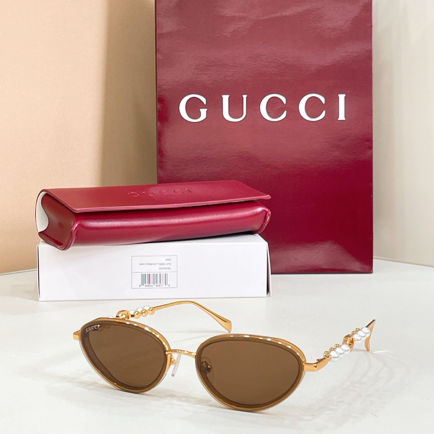 Gucci sunglasses with gold frame, dark brown lenses, round-oval shape and pearl details