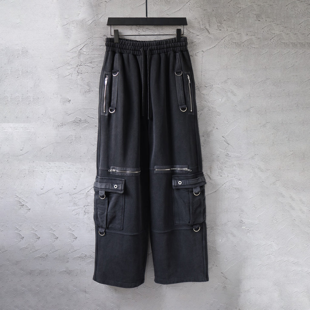 Cargo pants in dark fabric with elastic waistband and side utility pockets, zips, and straps