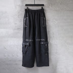 Cargo pants in dark fabric with elastic waistband and side utility pockets, zips, and straps