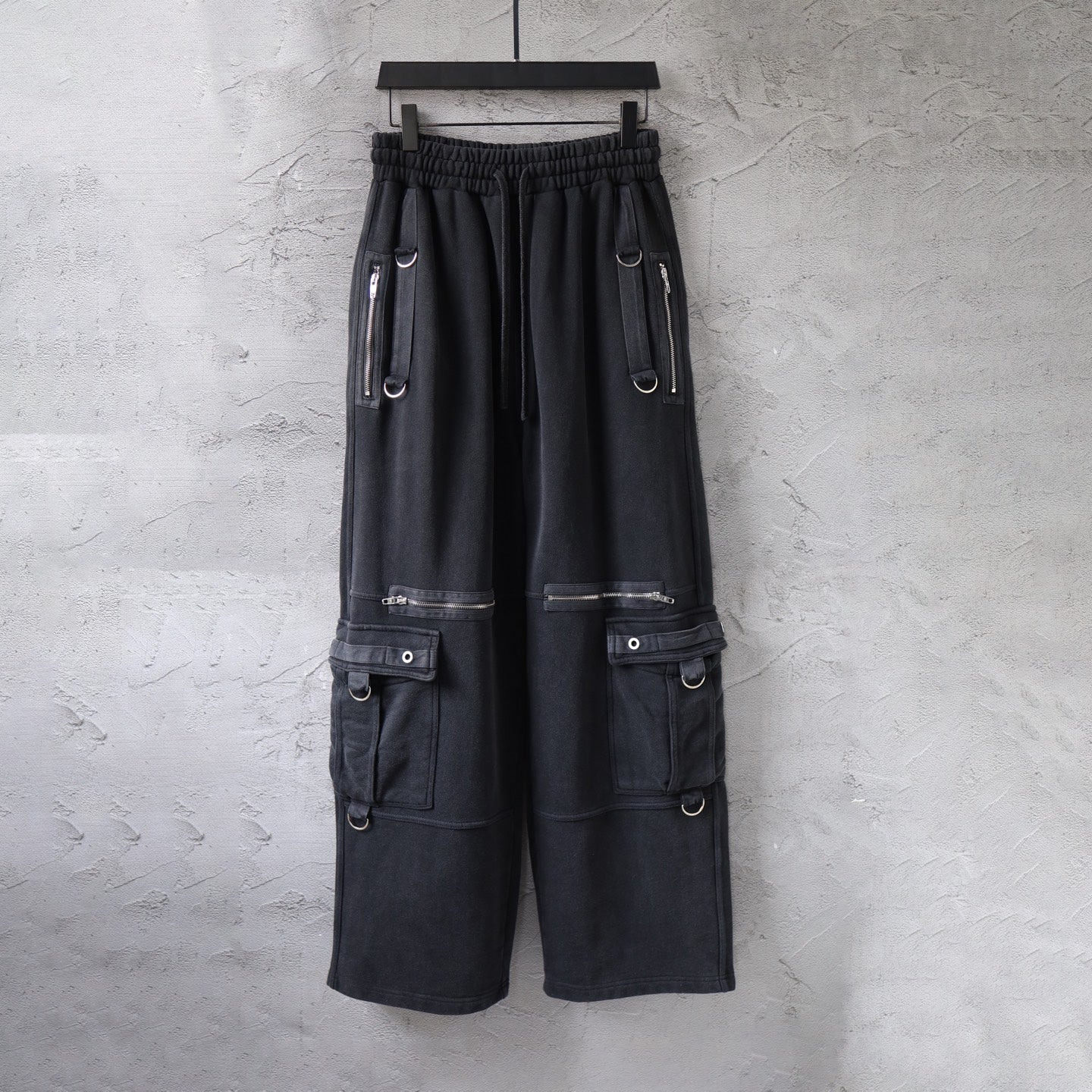 Cargo pants in dark fabric with elastic waistband and side utility pockets, zips, and straps