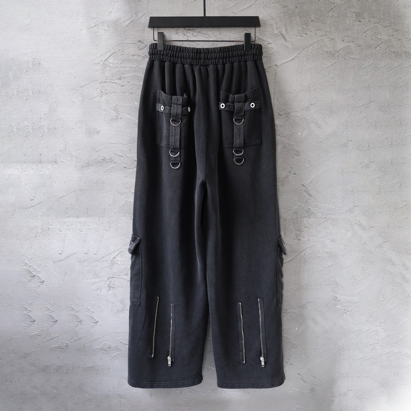 Dark cargo pants on hanger with elastic waistband, flap pockets, and hanging zipper pull tabs