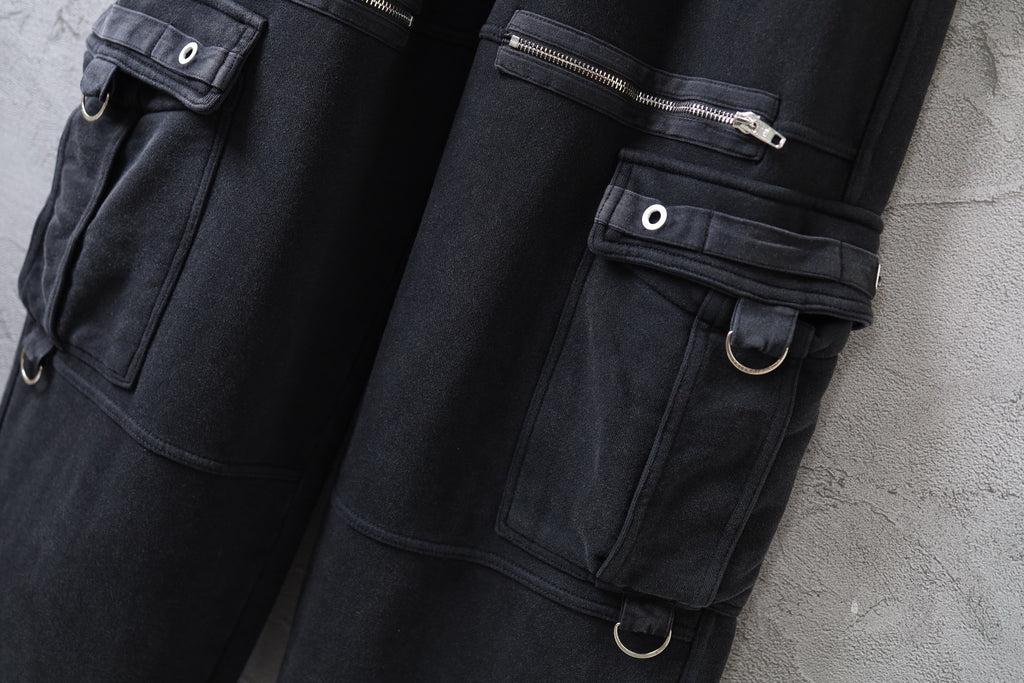 Close-up of dark cargo pants with flap pocket, snap button, and metal rings on strap