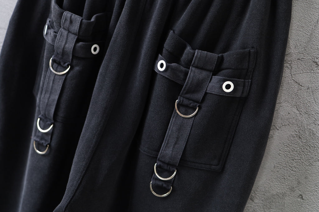 Close-up of dark cargo pants with flap pockets and metal ring straps with snap buttons