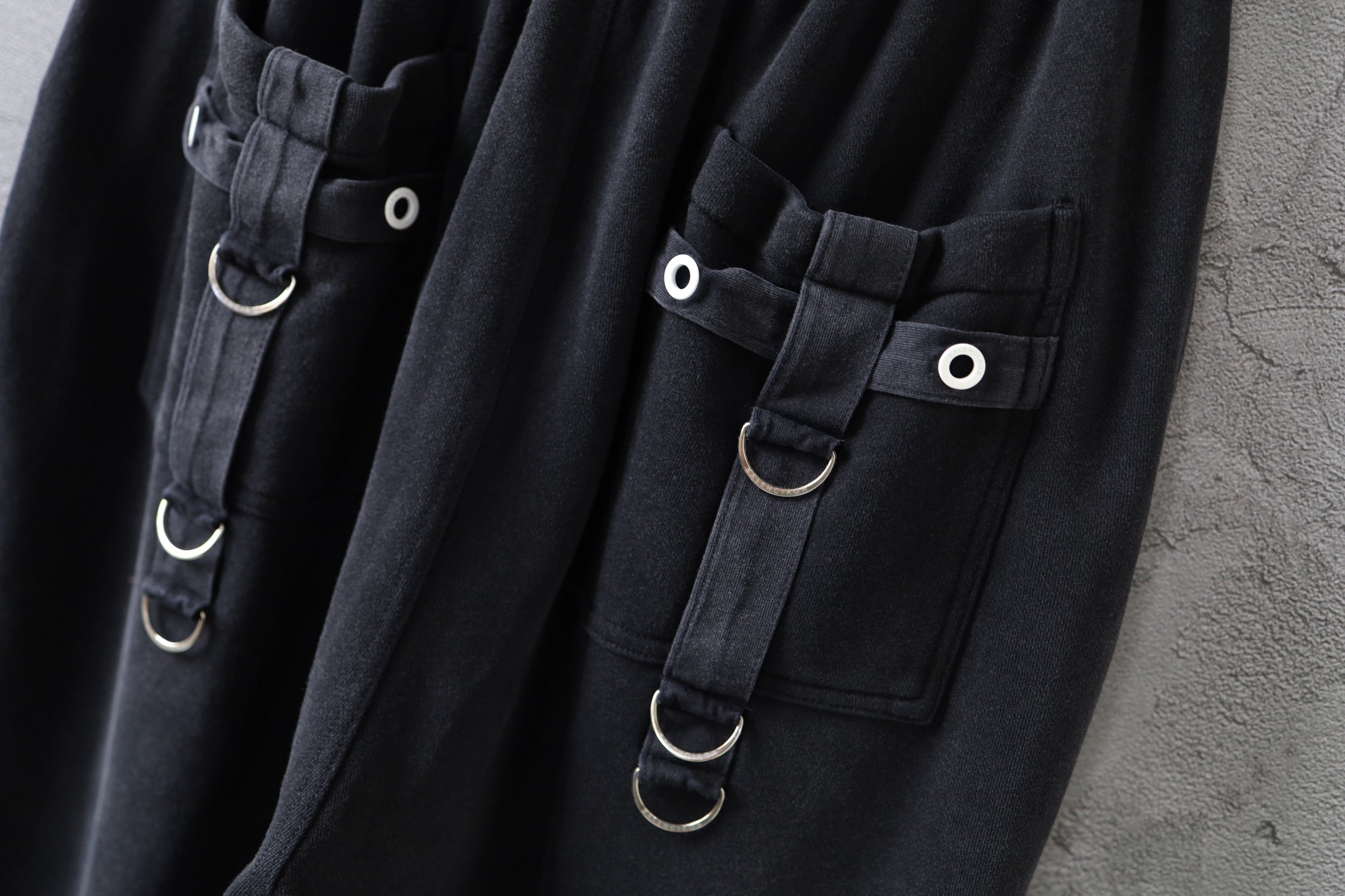 Close-up of dark cargo pants with flap pockets and metal ring straps with snap buttons