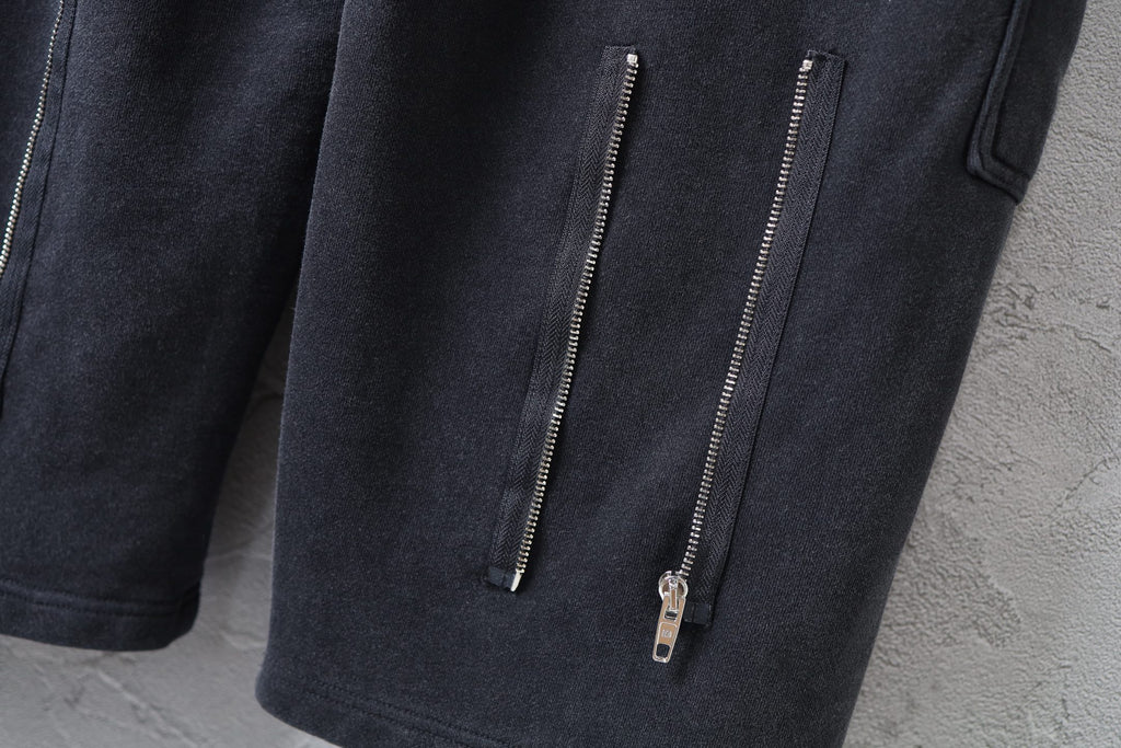 Dark cargo pants with two vertical zip pockets on the leg and metal zipper pulls