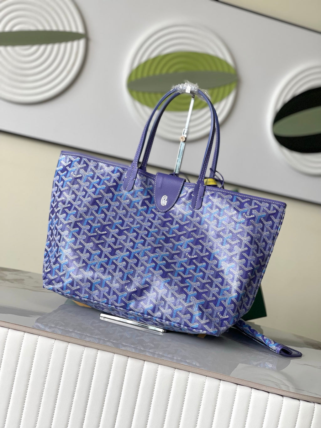 Blue patterned tote bag with top handles and front leather logo medallion