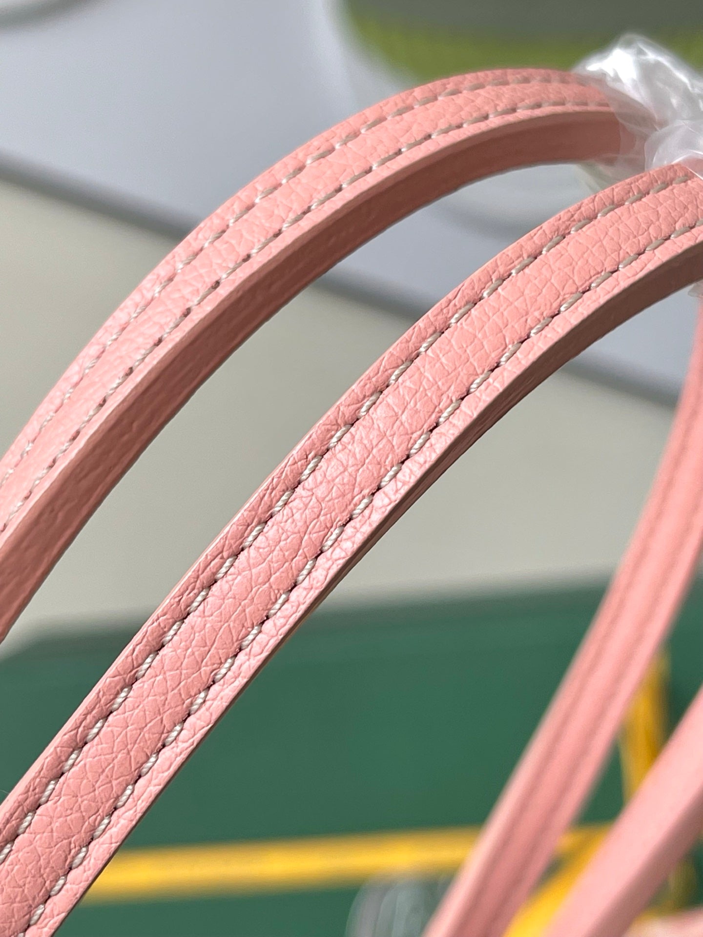 Pink leather tote handles with stitched seams on a patterned Goyard bag