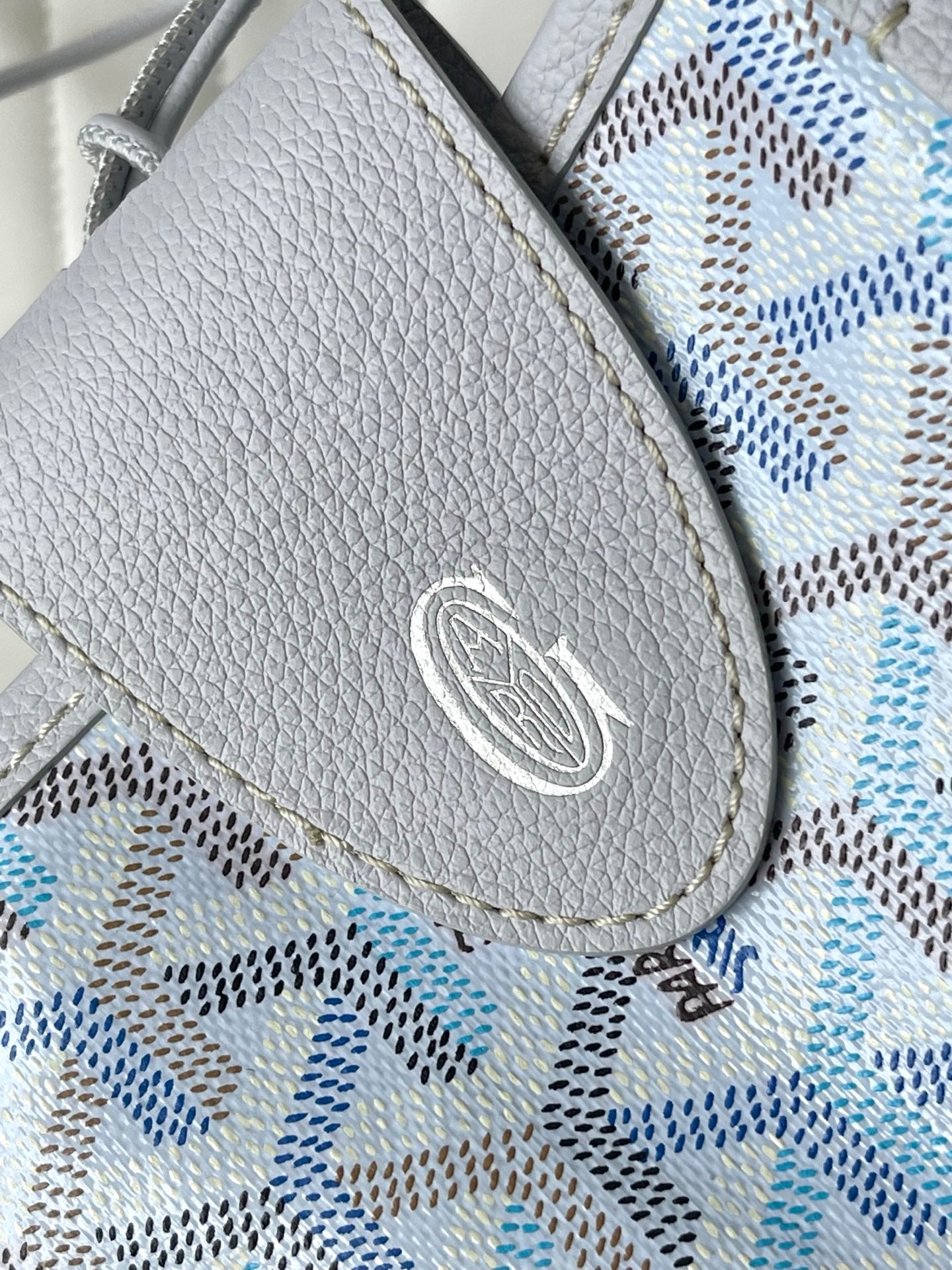 Close-up of light blue-and-white patterned flap pocket with silver logo emblem