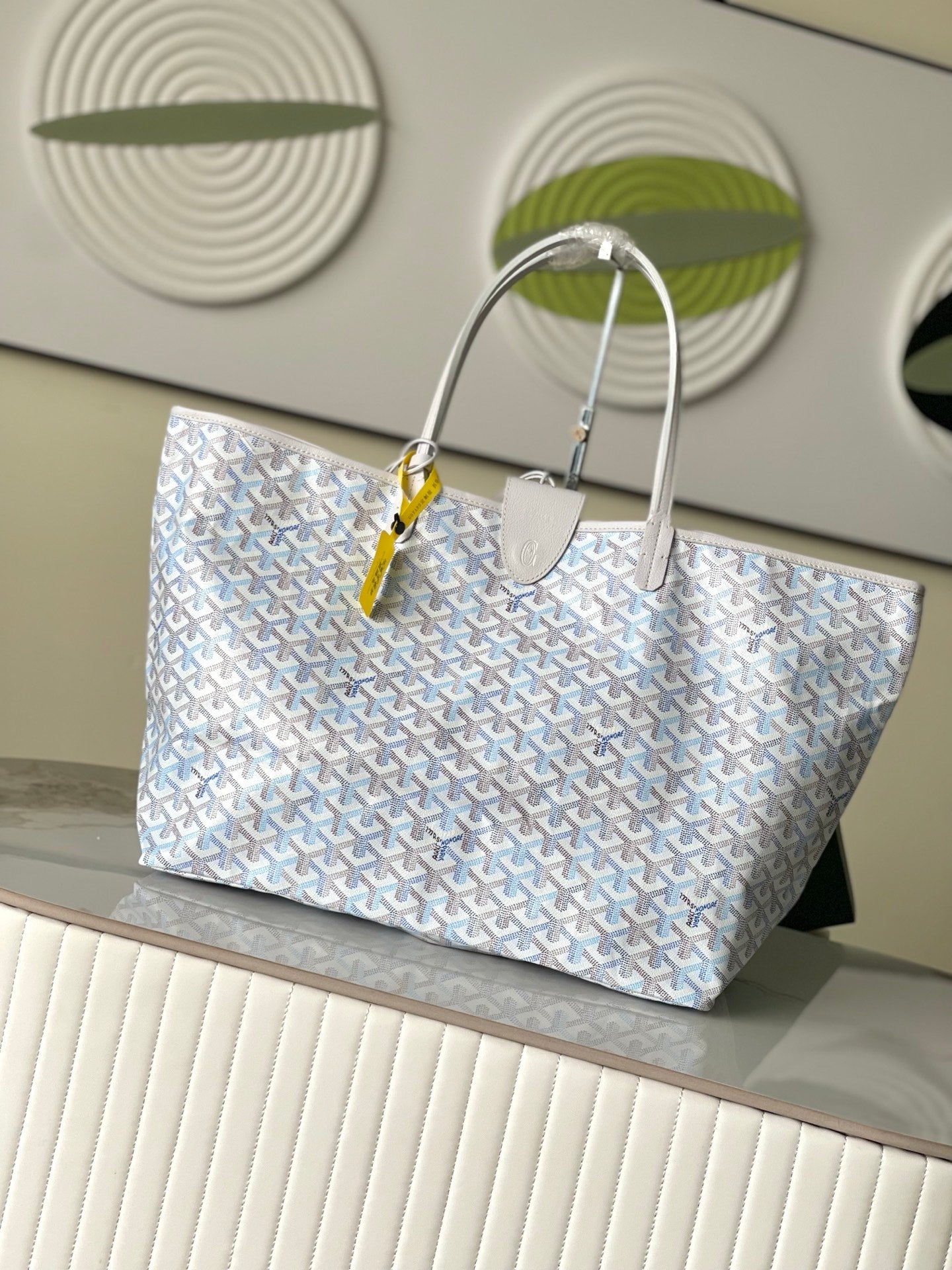Light blue patterned tote bag with long top handles and small luggage tag detail
