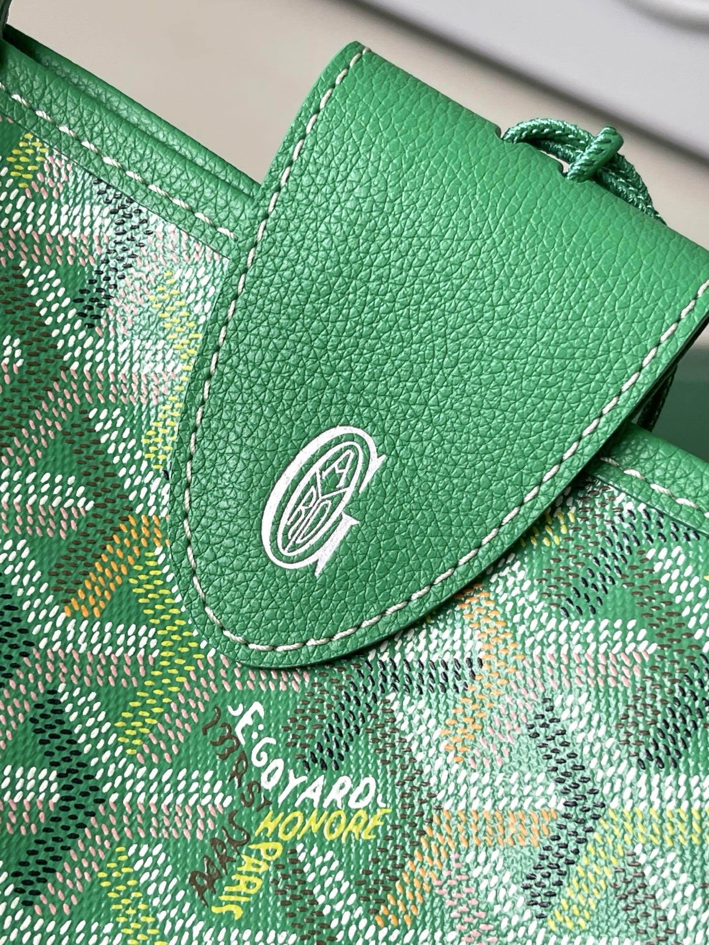 Green patterned tote bag flap with circular emblem and green leather stitching