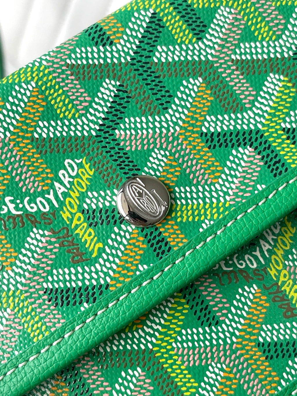 Green patterned tote bag with round metal clasp and stitched logo detail