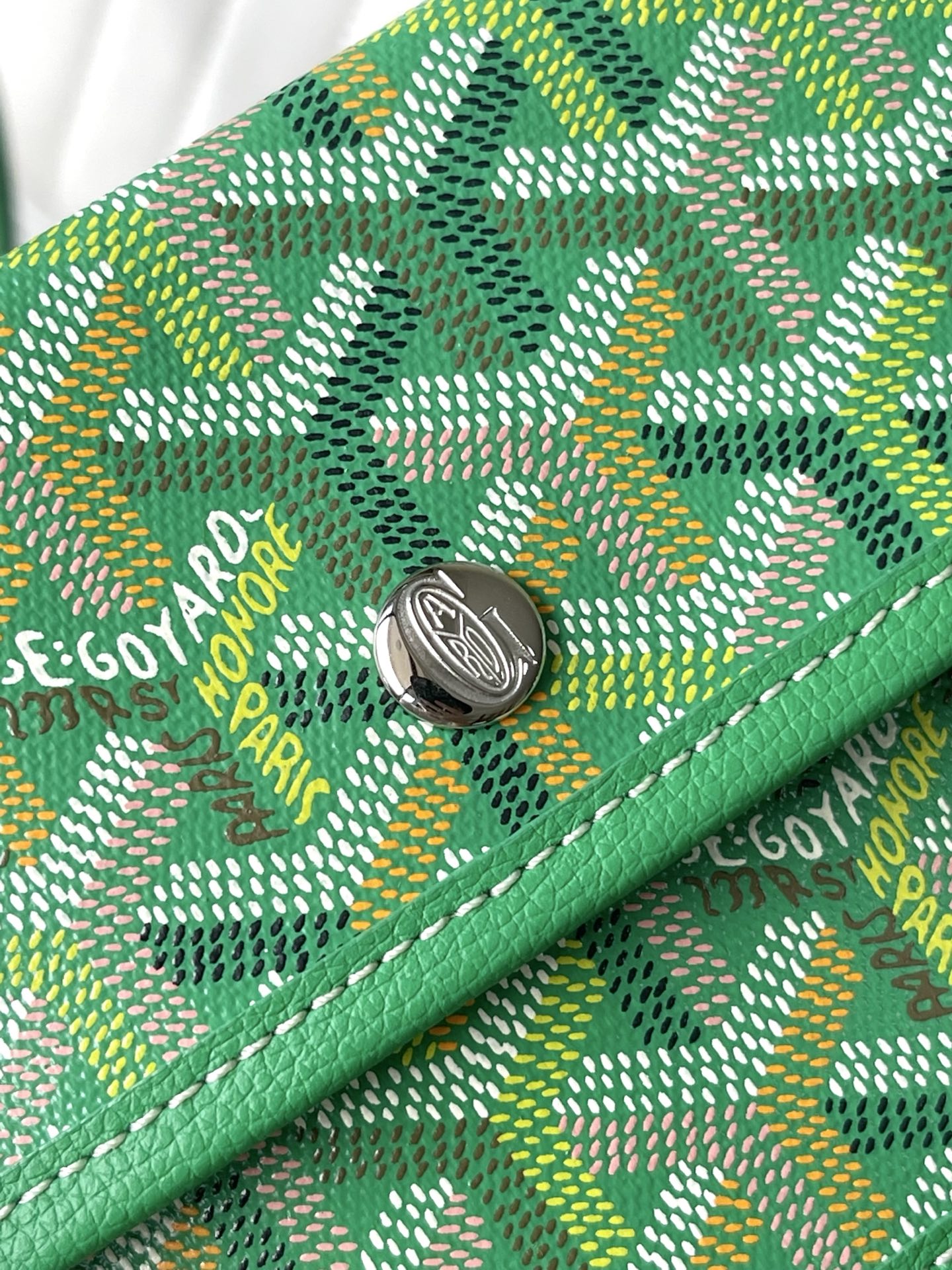 Green patterned tote bag with round metal clasp and stitched logo detail