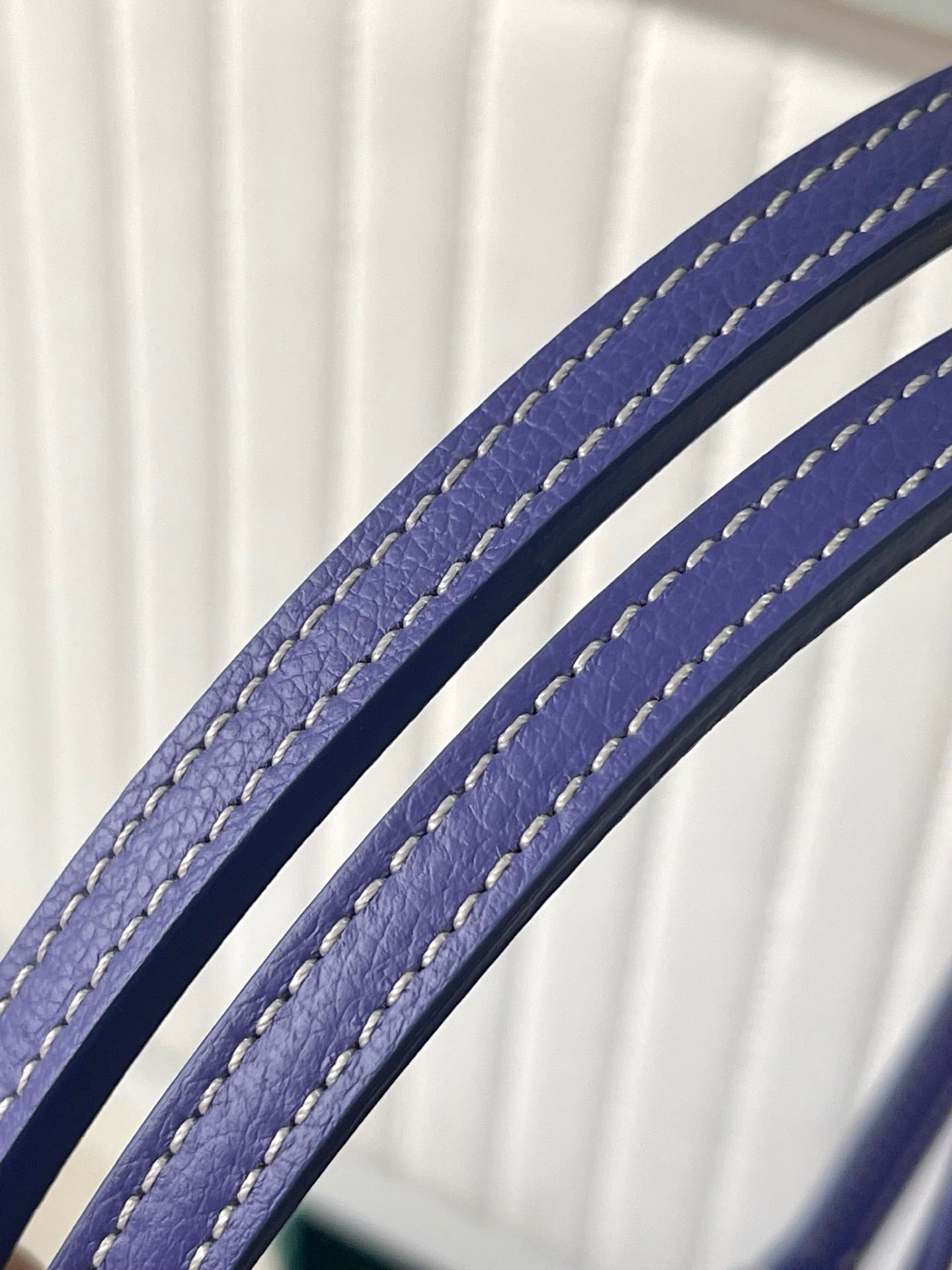 Blue leather carry strap with stitched edging on patterned Goyard bag