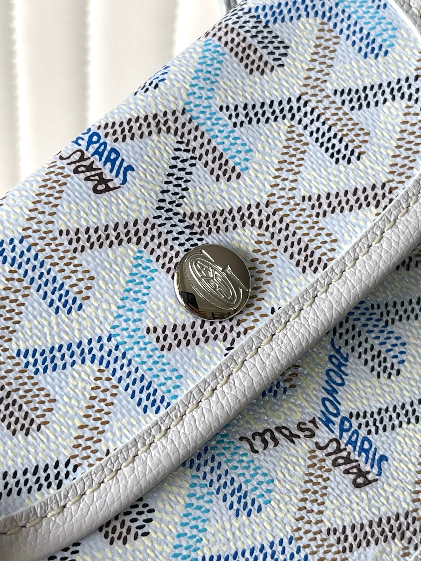 Light blue patterned pocket with round metal snap button and engraved charm