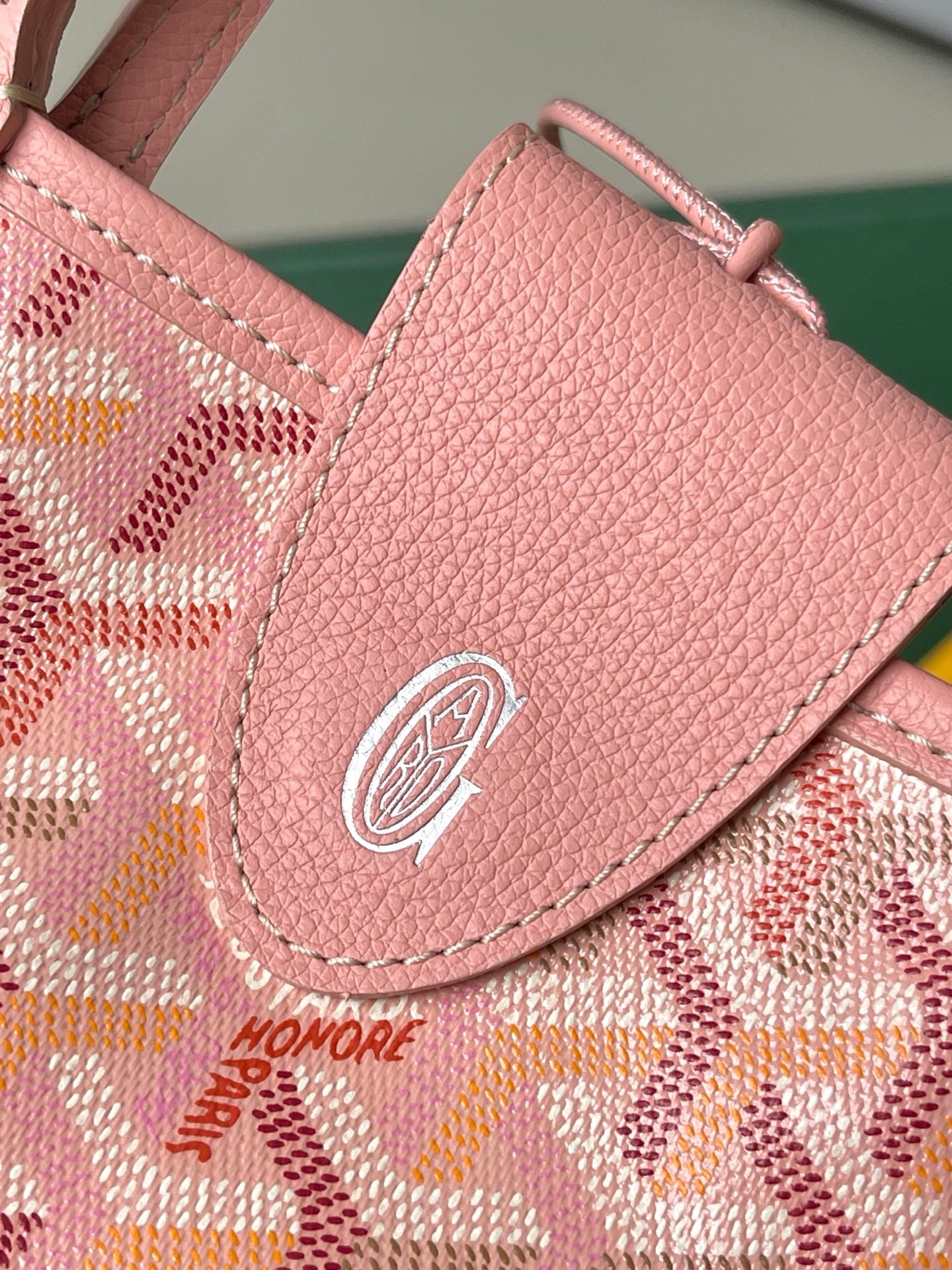Pink textured pocket flap with circular logo medallion and stitched edge detail.