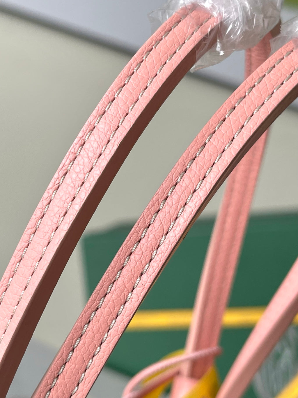 Pink leather bag handles with double stitching and glossy metal connector detail.