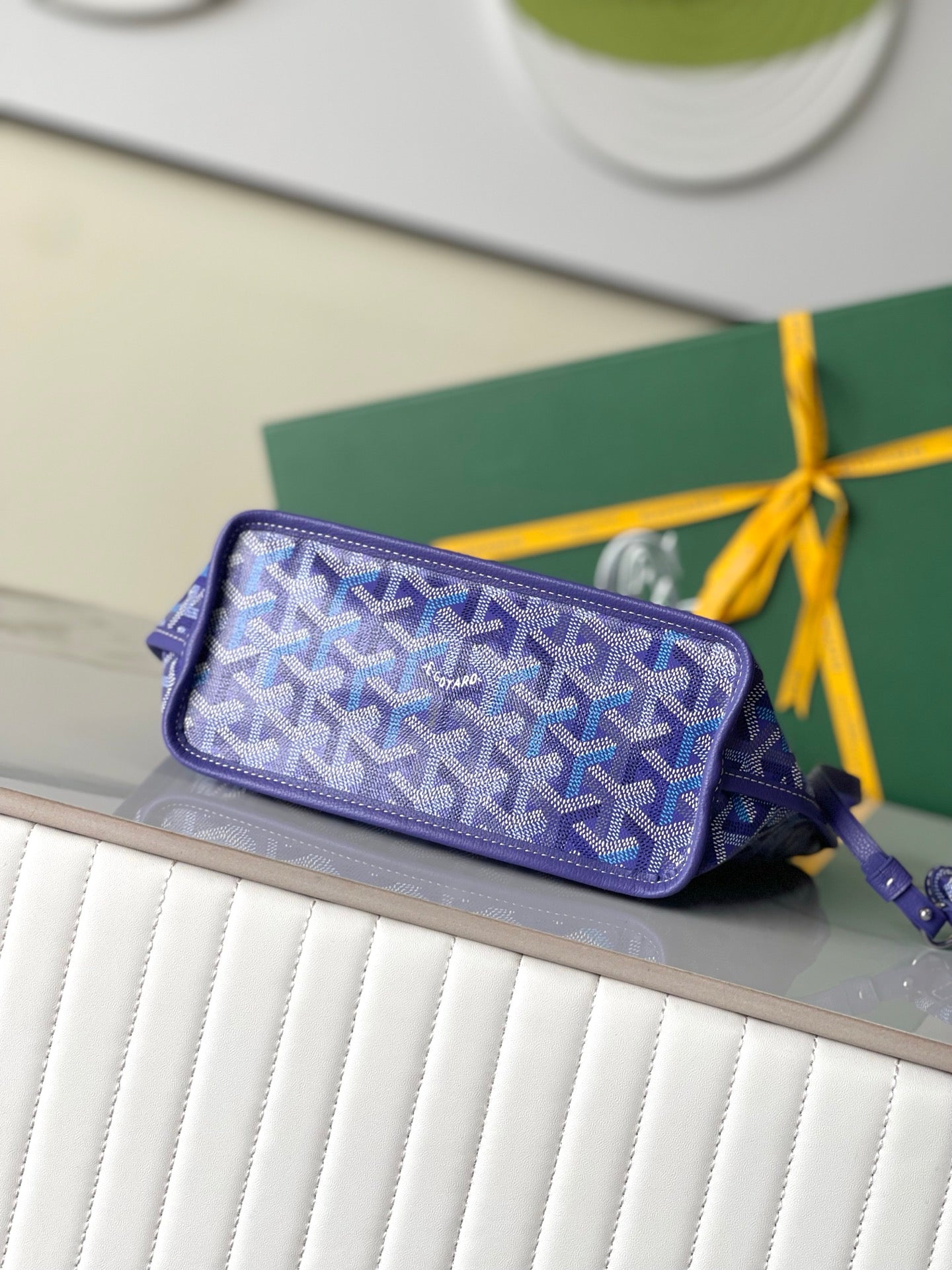 Goyard patterned zip pouch in blue with wrist strap on glass shelf
