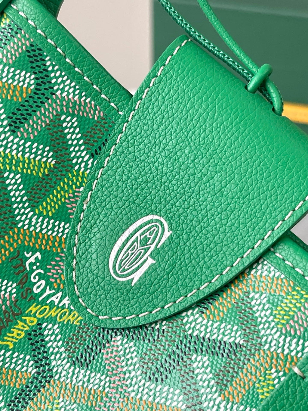 Green Goyard leather flap with metal emblem snap and stitched trim over patterned fabric