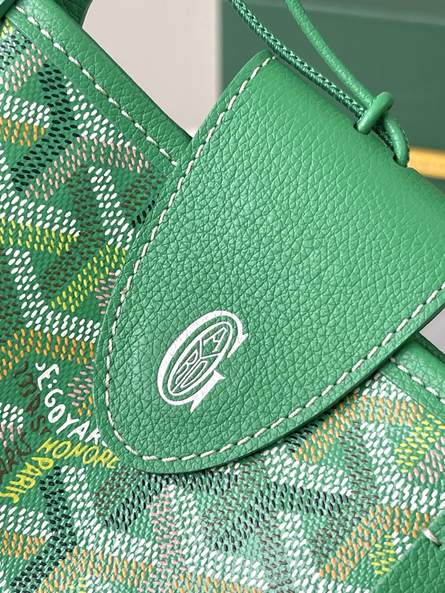 Green Goyard leather flap with metal emblem snap and stitched trim over patterned fabric