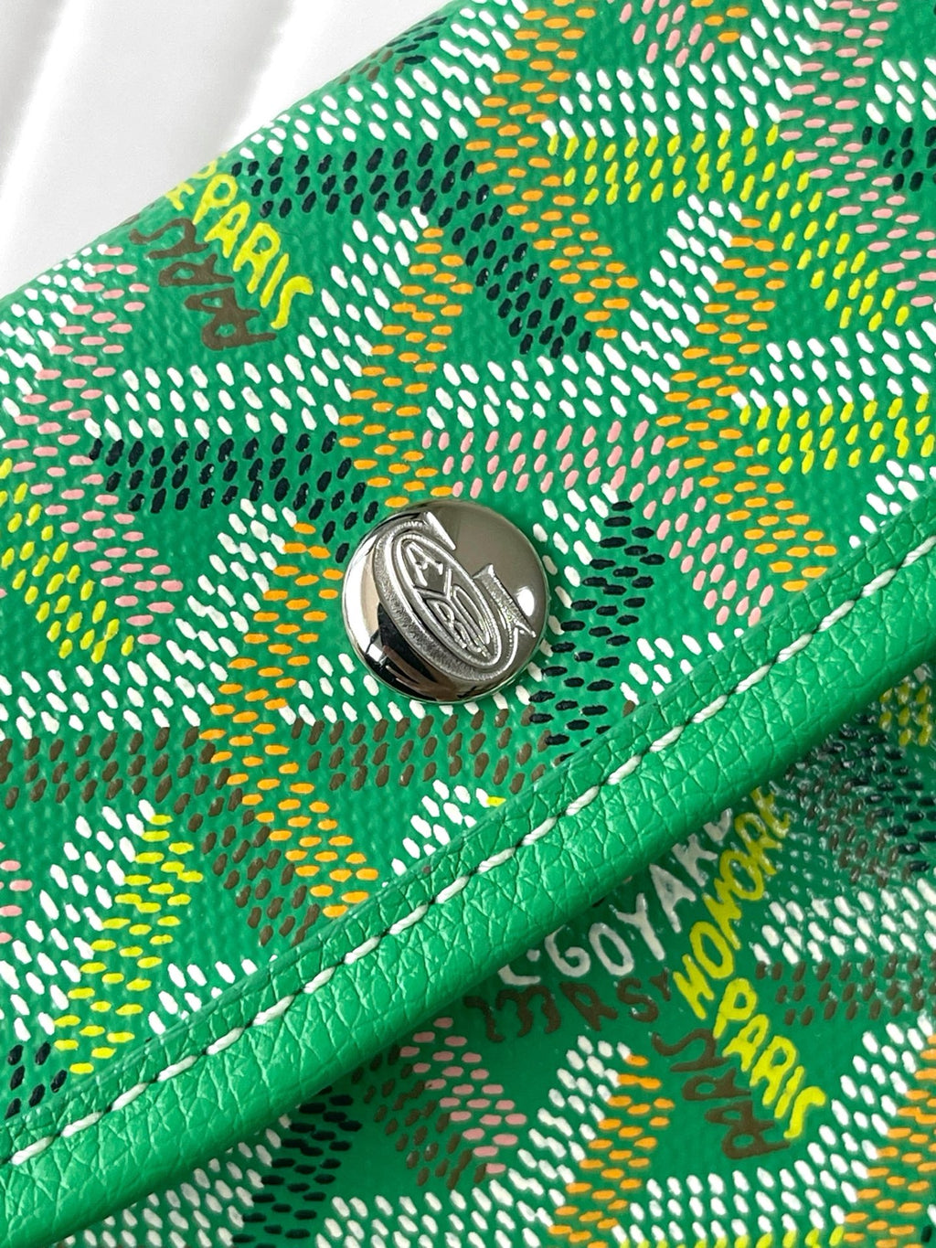 Green Goyard patterned fabric wristlet with round metal snap button and stitched border