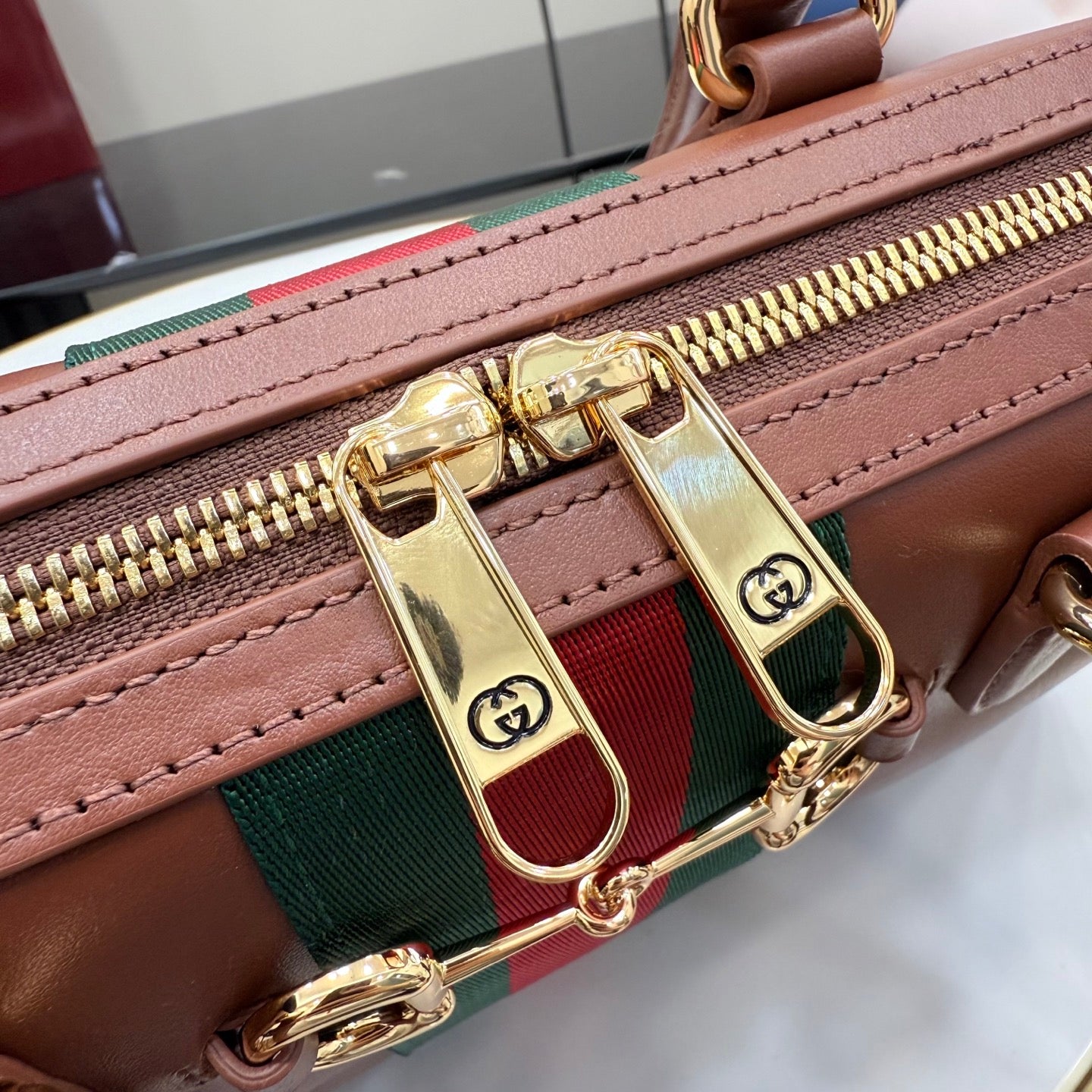 Brown leather bag with green-and-red stripe and gold zipper pull.