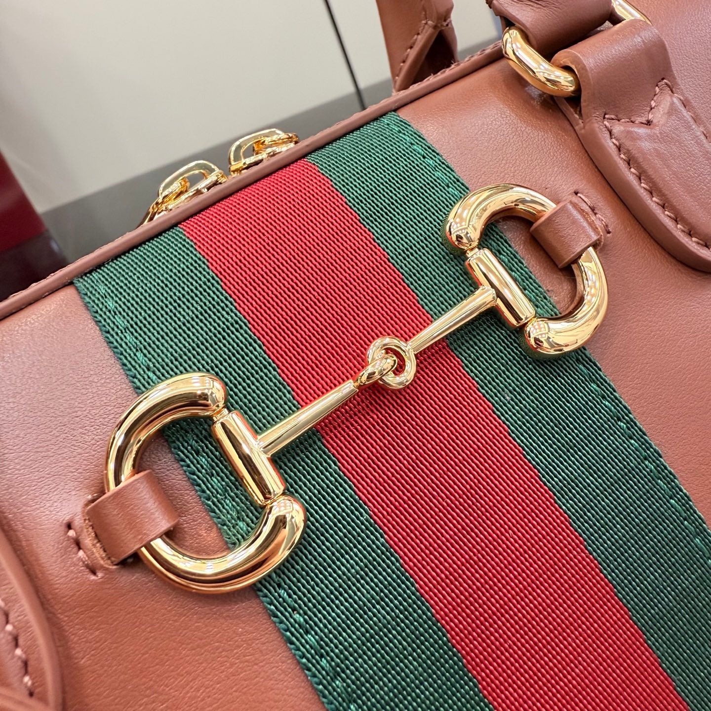 Brown leather bag detail with green-and-red web and gold double-link hardware.