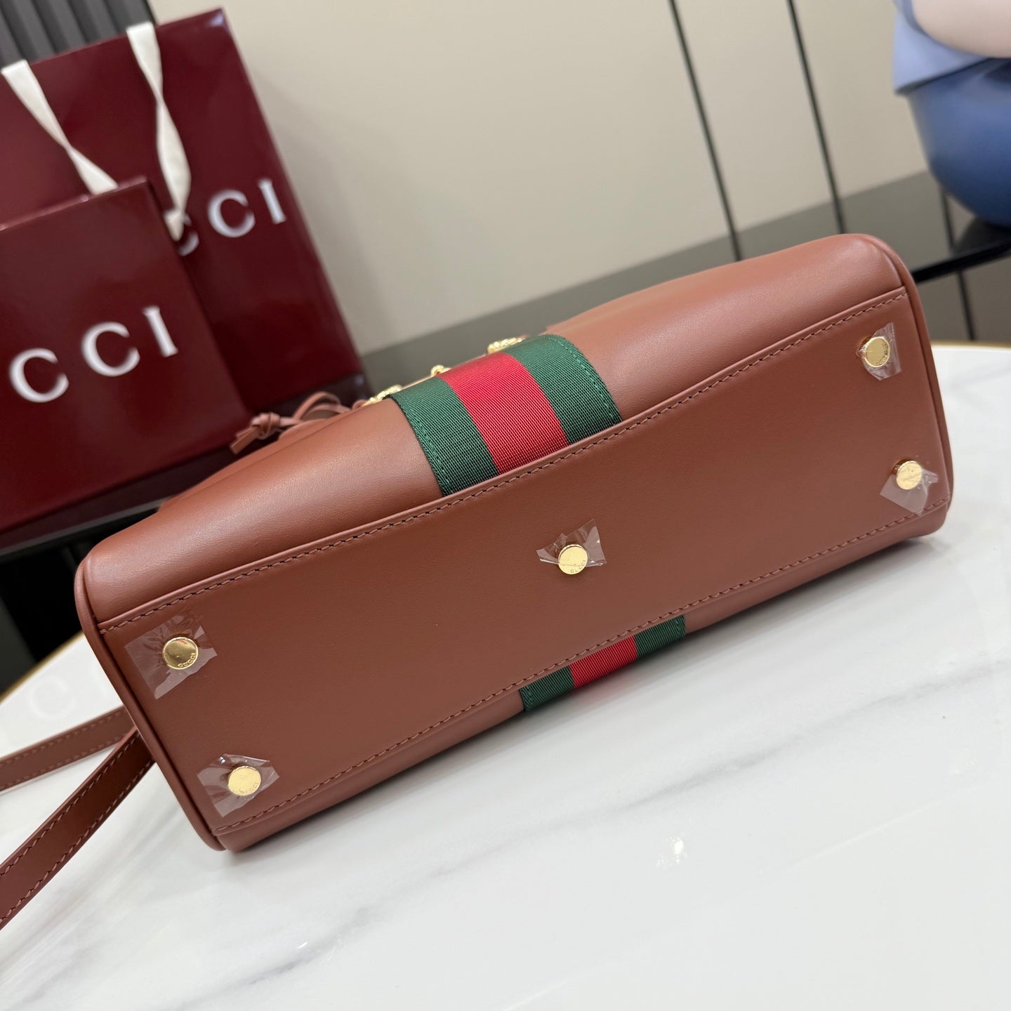 Brown leather clutch-style bag with green-and-red web stripe and gold studs.