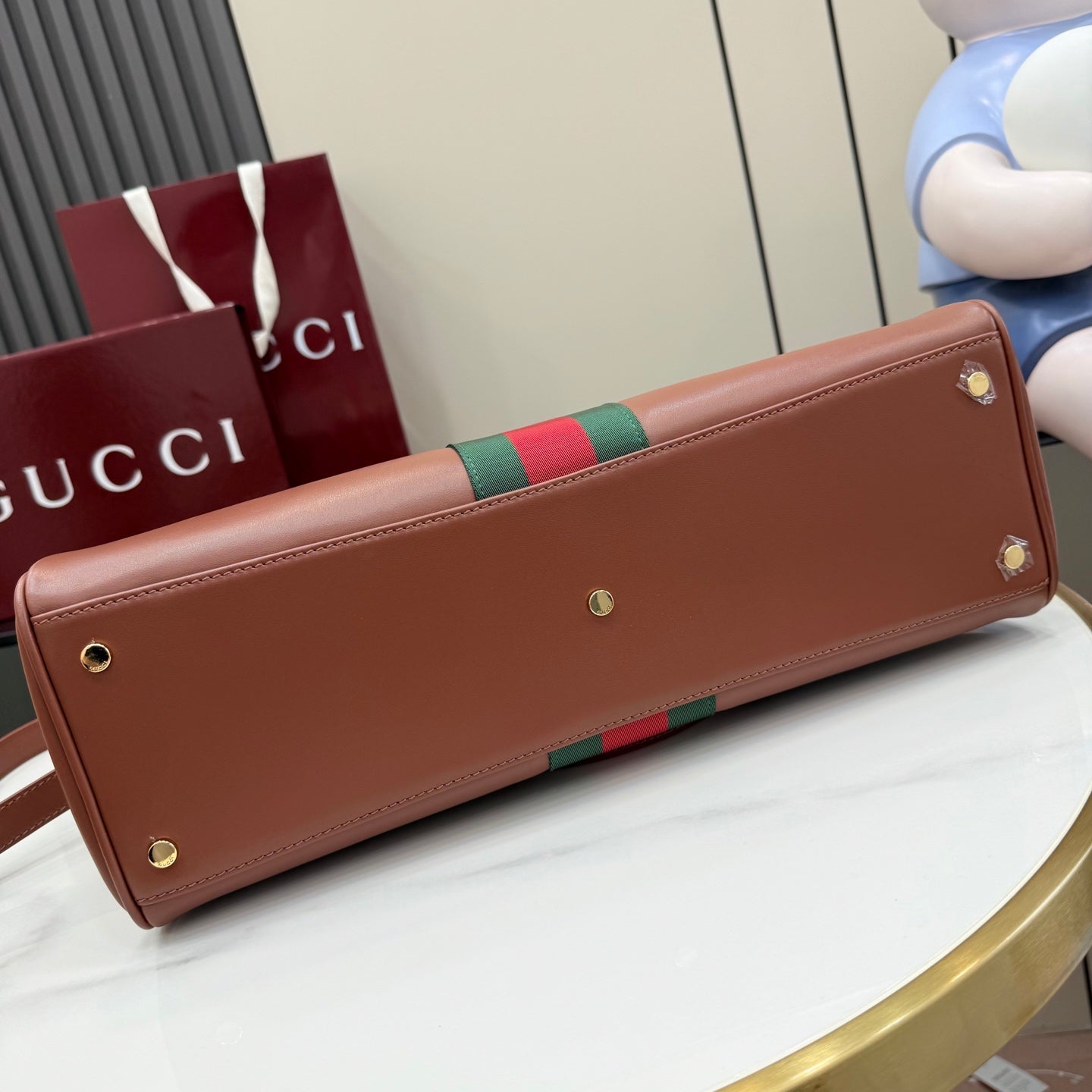 Brown Gucci tote with gold studs along side, featuring green-and-red web stripe detail