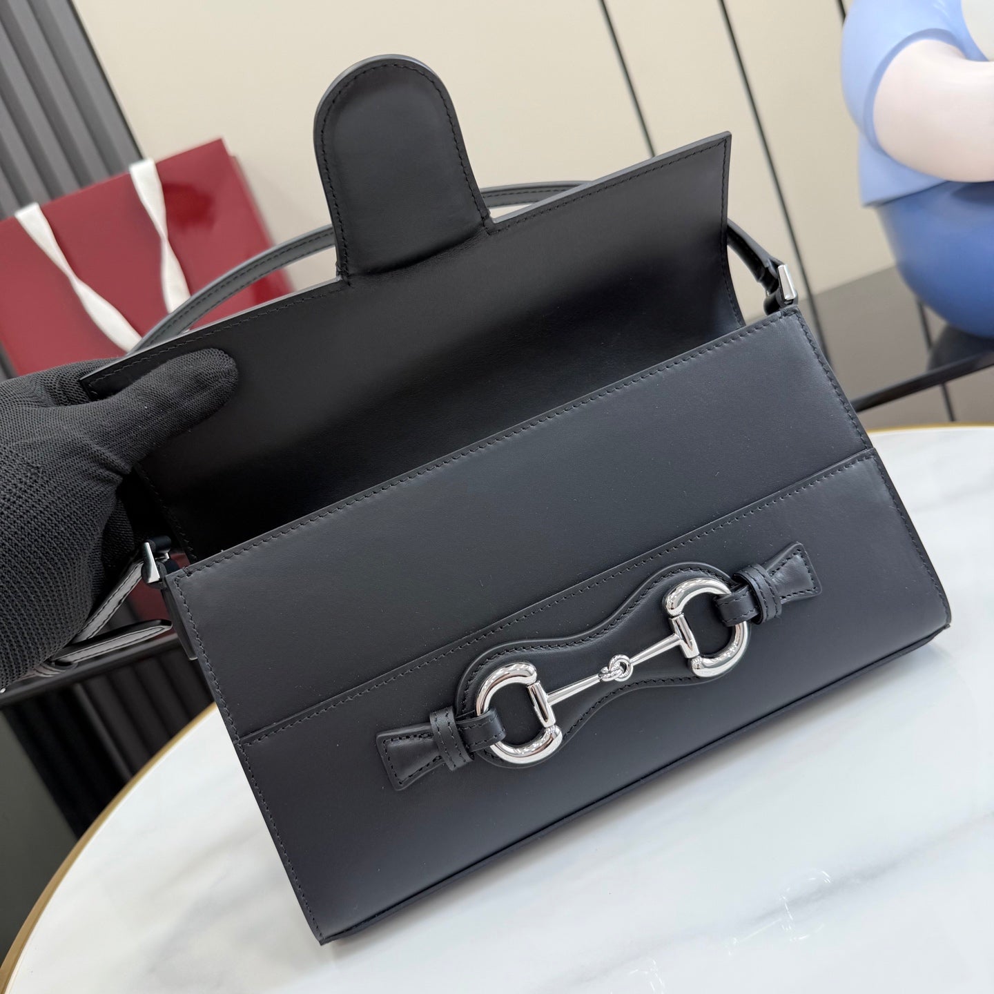 Black leather shoulder bag with flap, top handle, and silver-tone horsebit front clasp