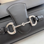 Black leather bag detail showing silver-tone horsebit clasp and stitched flap panel
