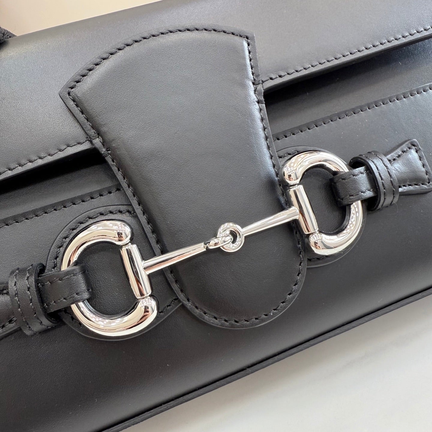 Black leather bag detail showing silver-tone horsebit clasp and stitched flap panel