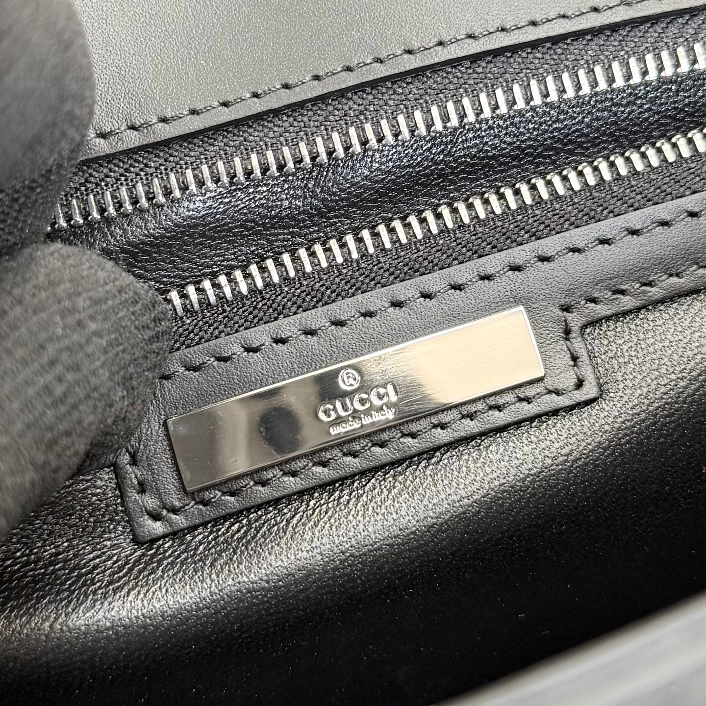 Black leather bag zipper with Gucci logo metal tab and close-up of stitched trim