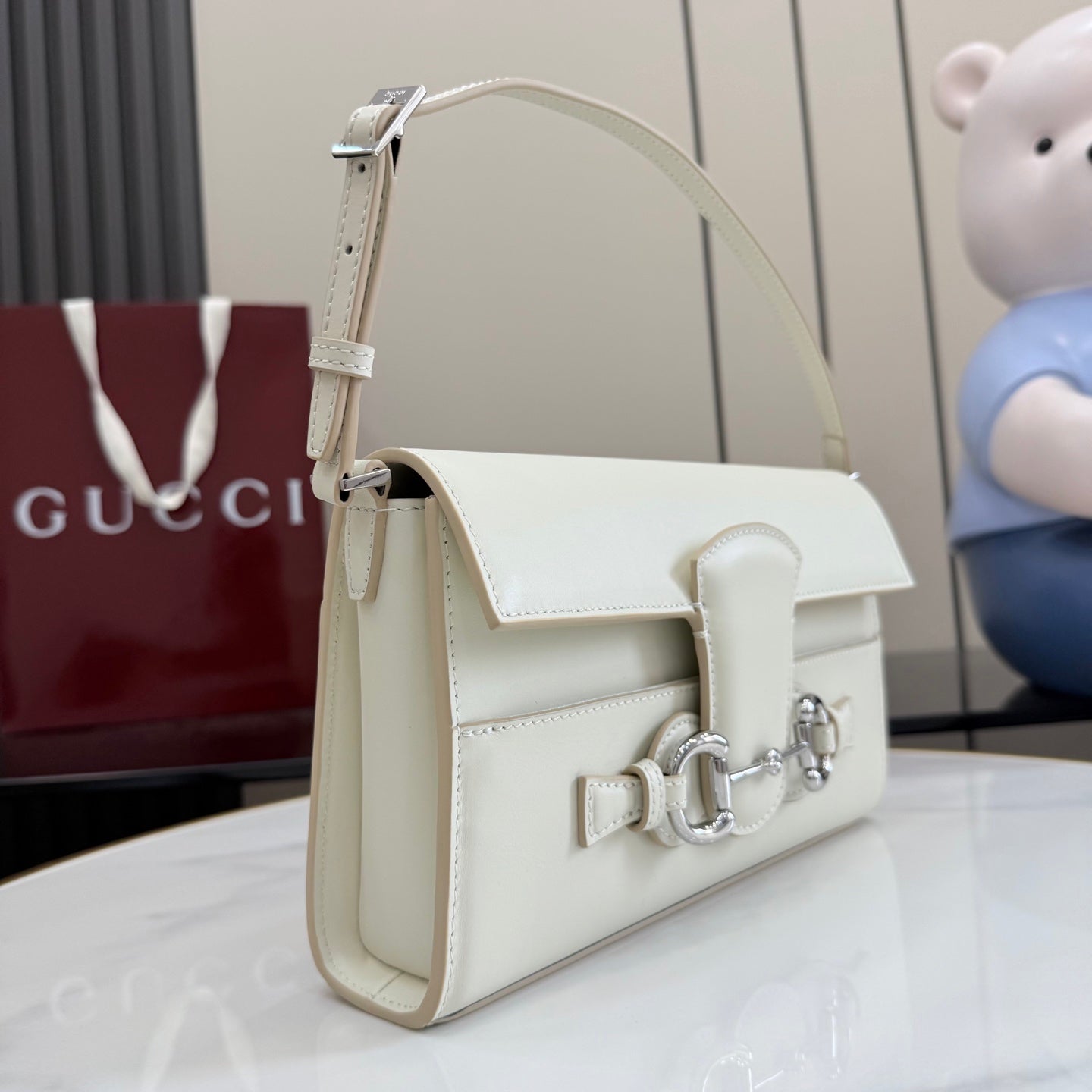 Cream top-handle shoulder bag with flap closure, front strap hardware, and curved handle