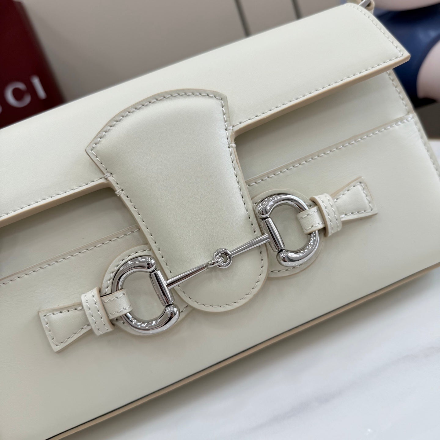Cream shoulder bag close-up of front flap, D-ring hardware, and strap connector