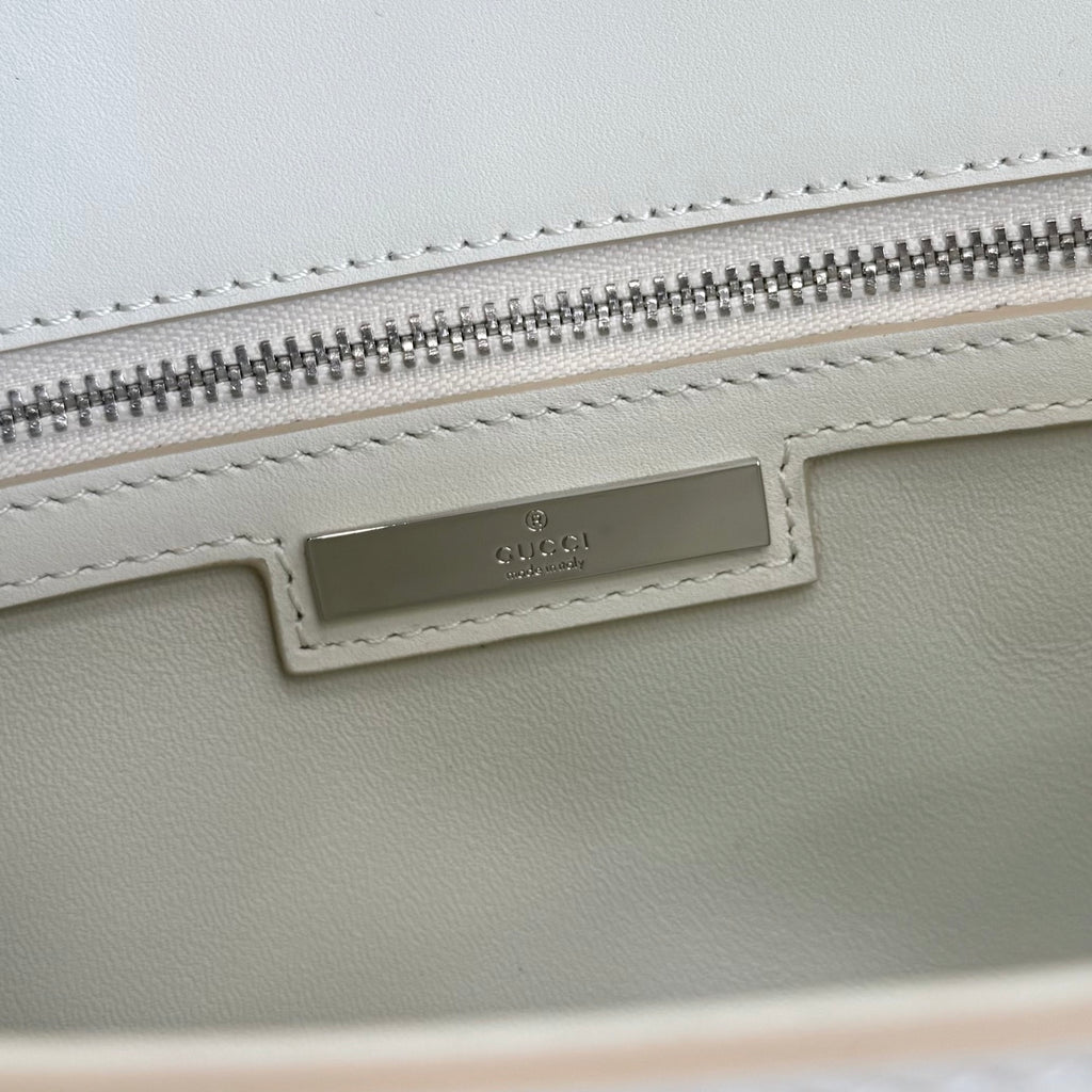 Cream bag with stitched label and silver zipper on the top edge