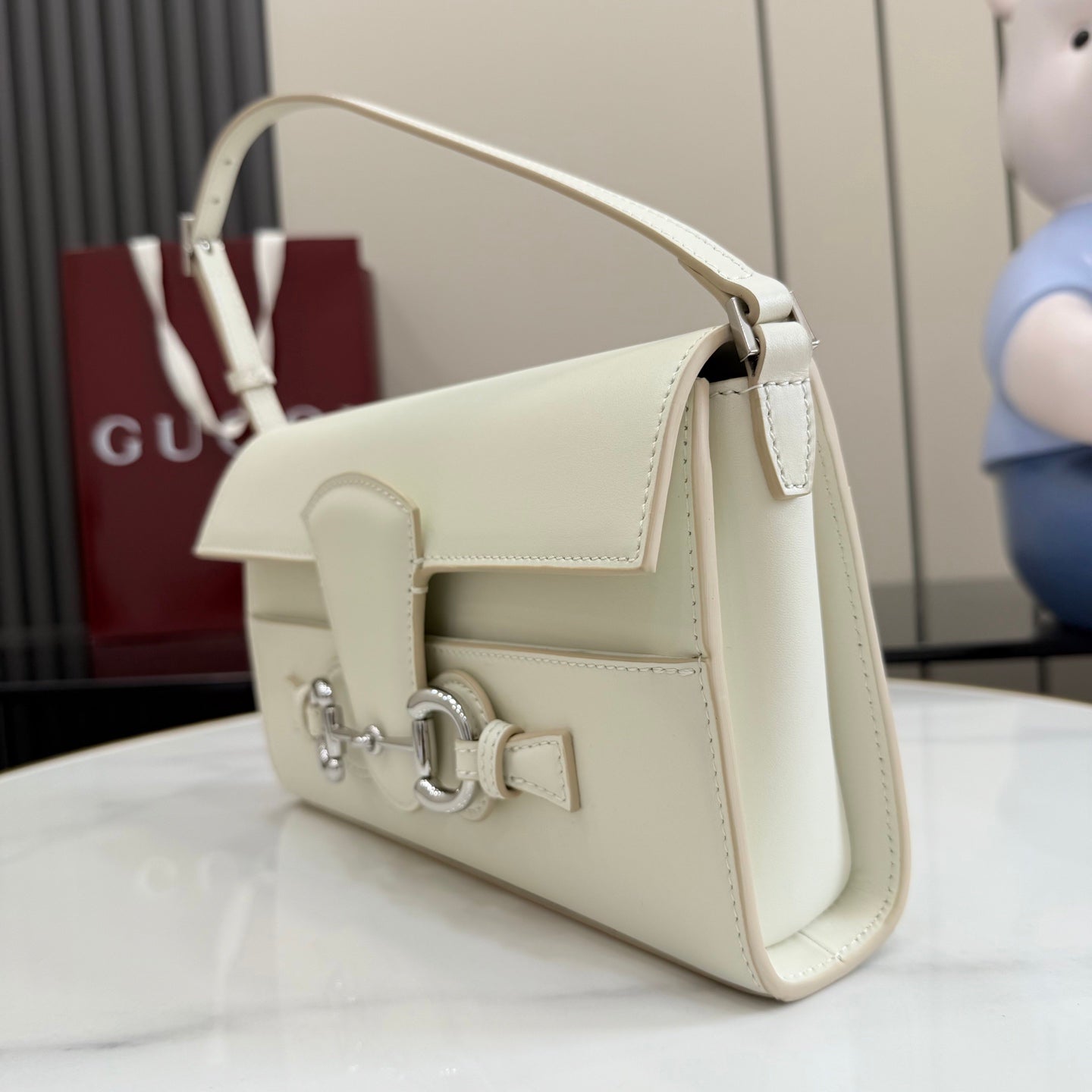 Cream shoulder bag shown from side angle with curved top handle and flap detail