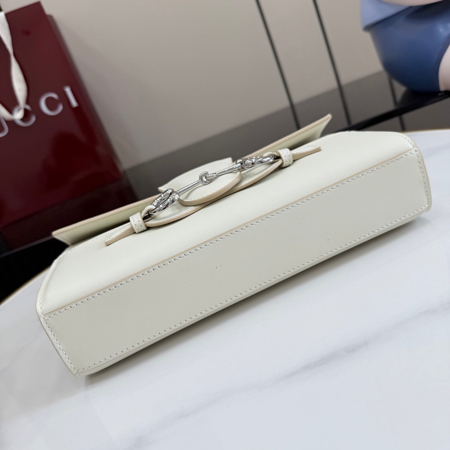 Cream handbag with metal clasp hardware and slim side profile along the strap
