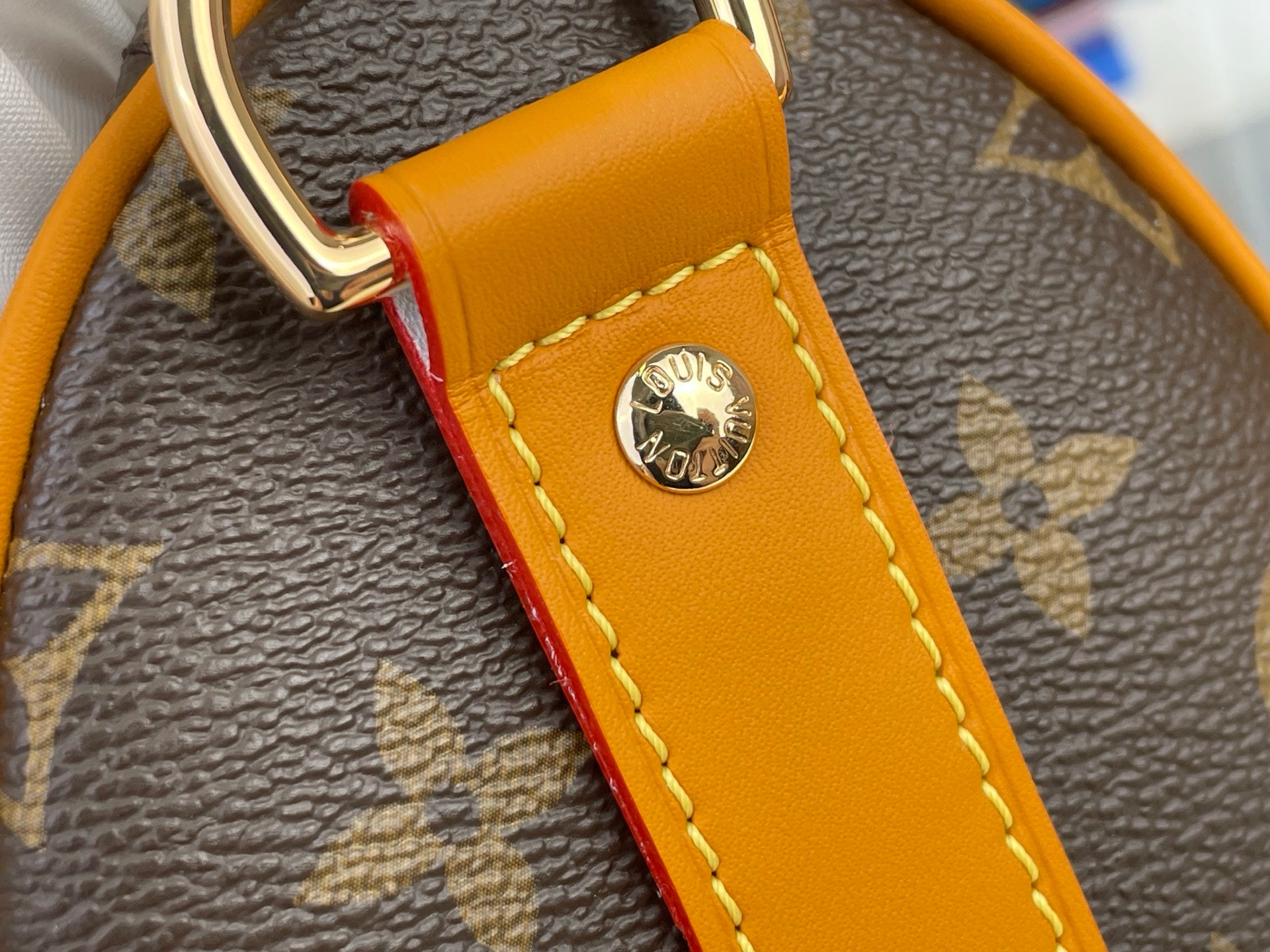Louis Vuitton monogram bag detail with orange leather tab and round gold emblem