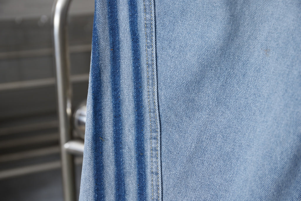 Light blue denim fabric with stitched panel seams and vertical pocket edge
