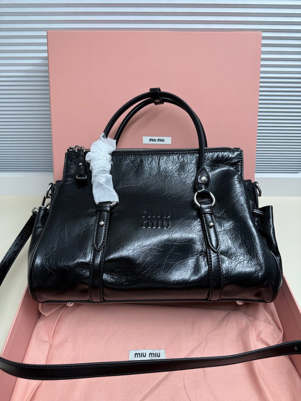 Black leather satchel with top handles, side tabs, and detachable crossbody strap