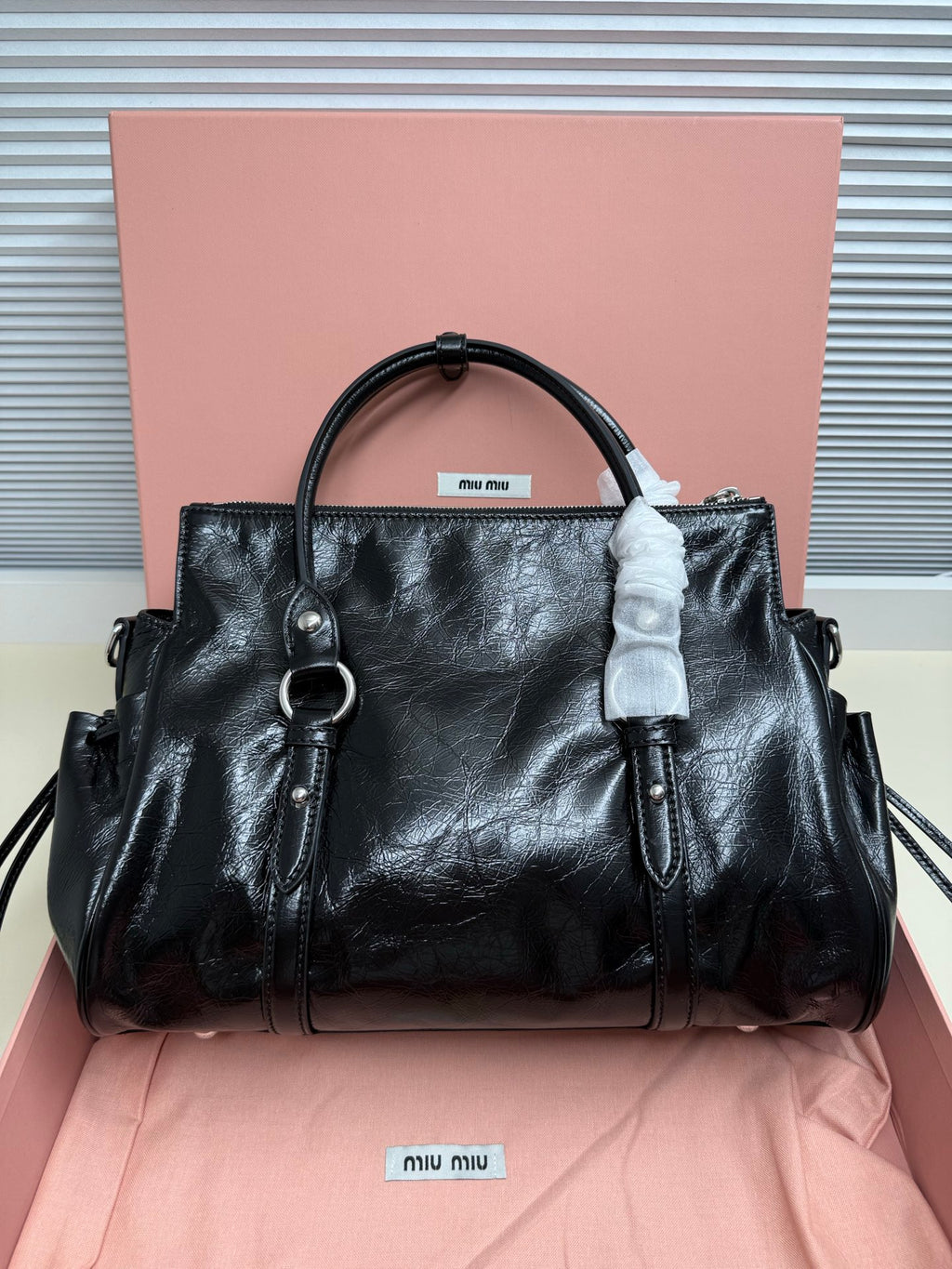 Black leather handbag with top handle, side rings, and front seam detail