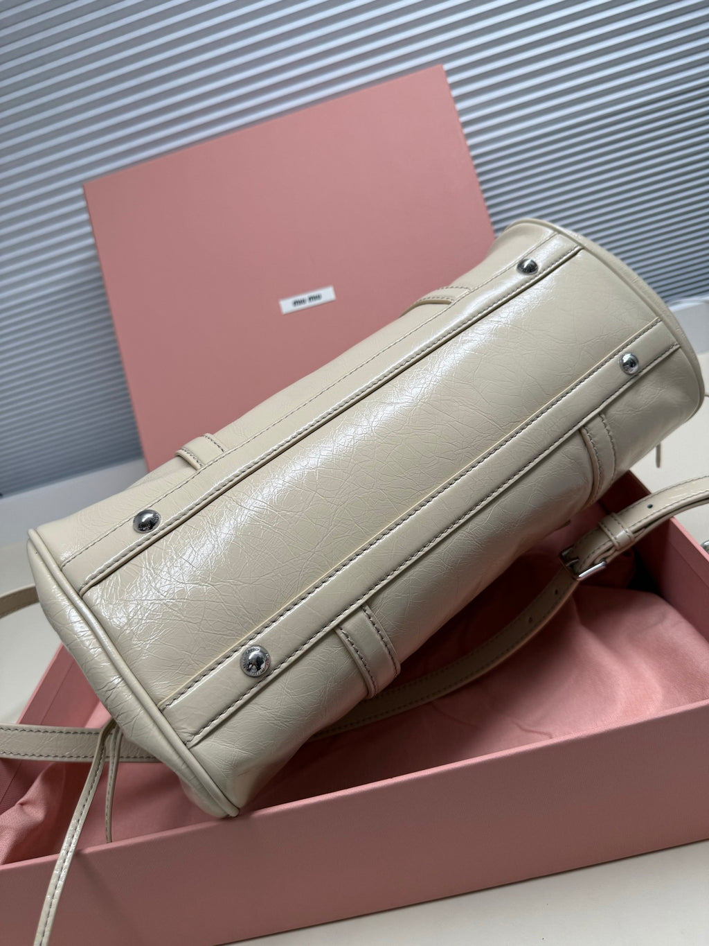 Ivory leather handbag with top zipper, front panel seams, and silver-tone studs