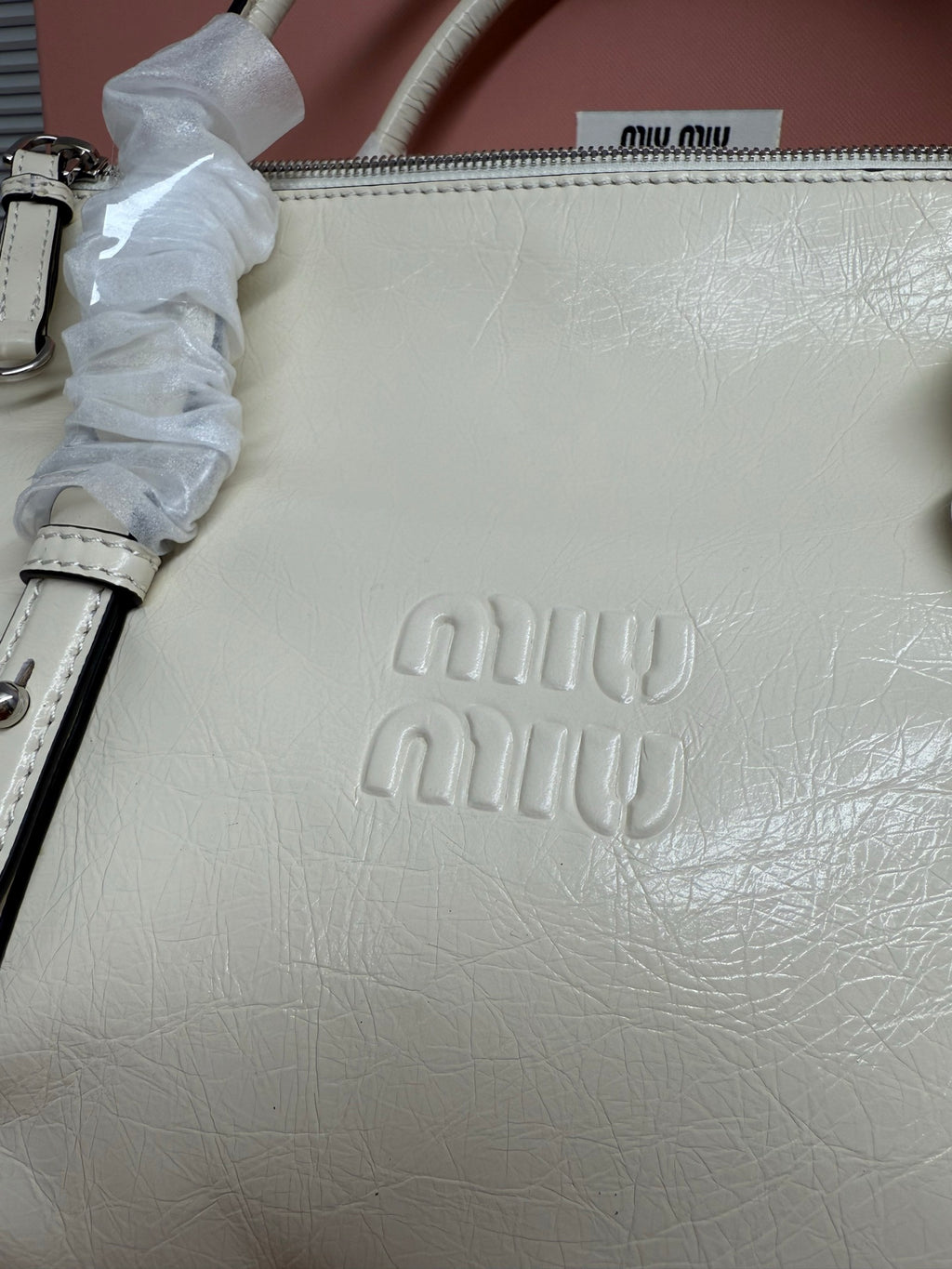 White leather handbag close-up with embossed miu miu logo and top zipper